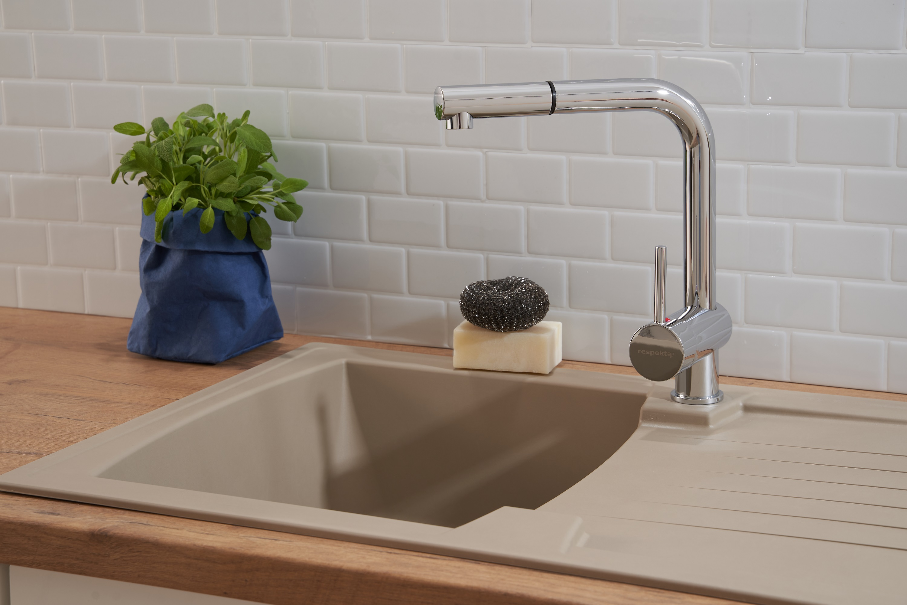 Ein modernes Küchenbecken mit Wasserhahn, Seife und einer Pflanze in einer blauen Tüte.
