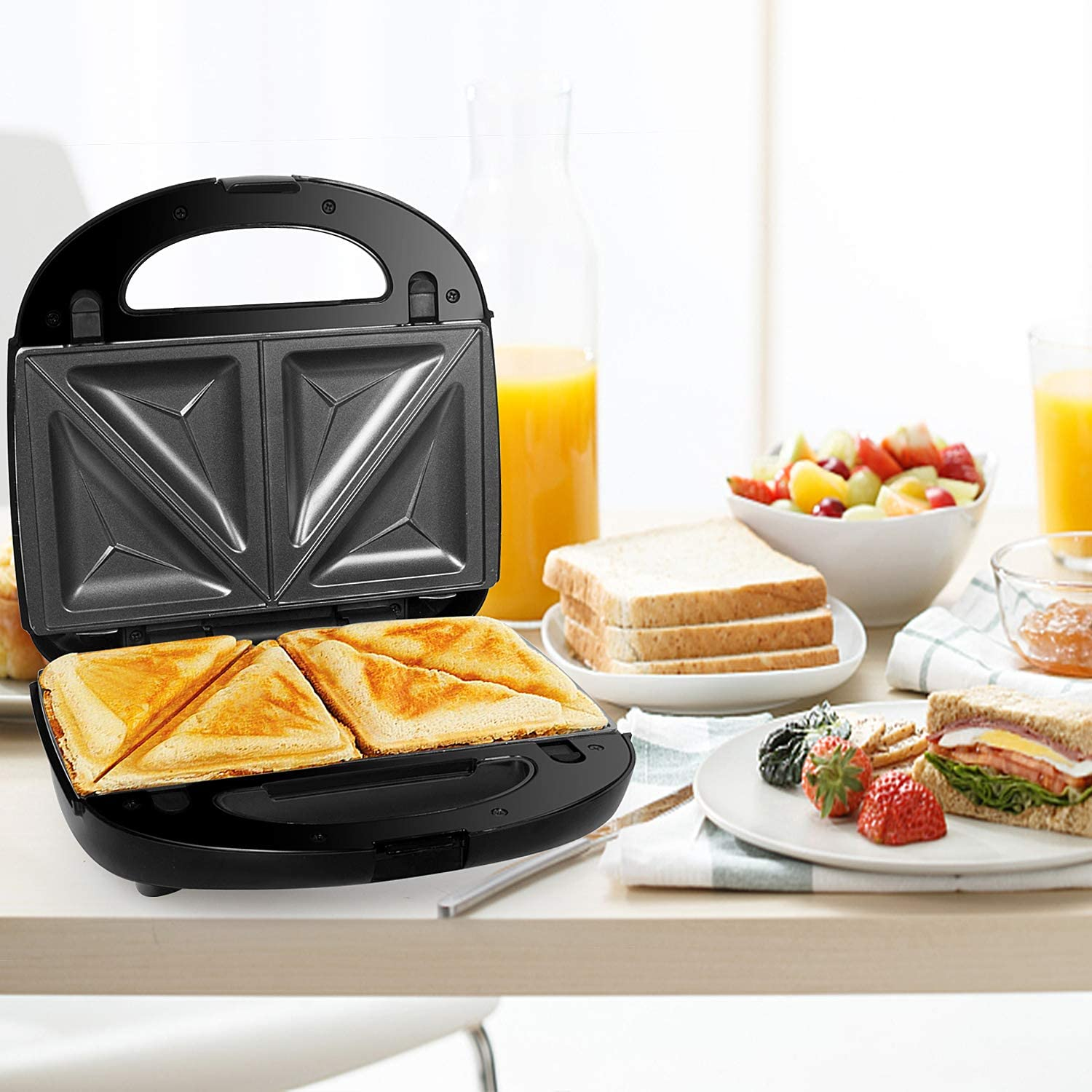 Ein schwarzer Sandwichmaker mit Sandwiches und Obst. Weißer Hintergrund.