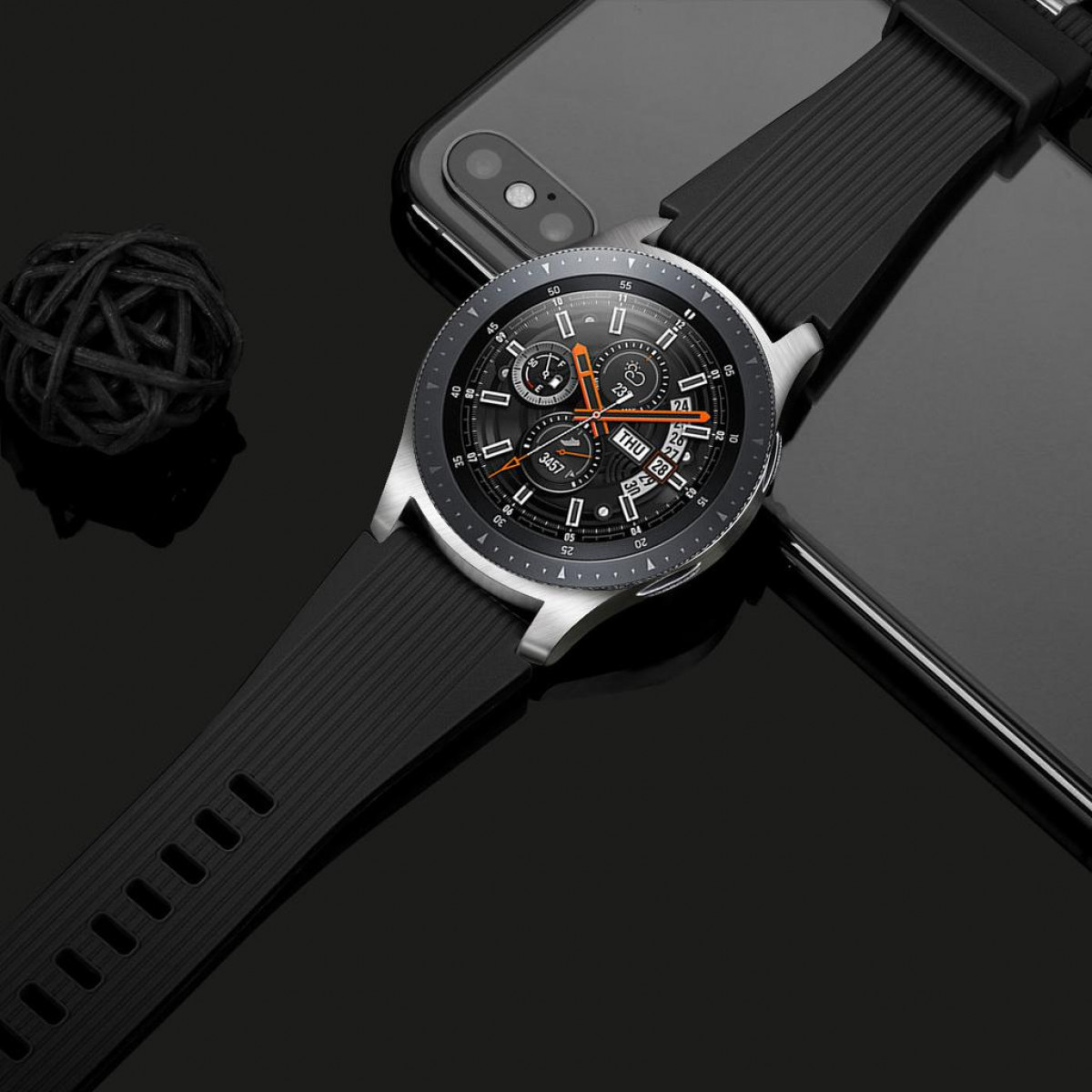 Eine schwarze Smartwatch auf einer reflektierenden Oberfläche. Ein Telefon und ein dekorativer Ball sind ebenfalls darauf.