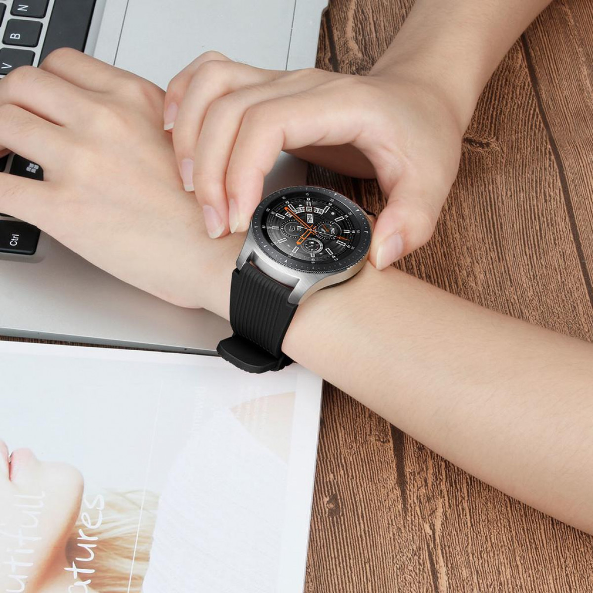 Hand mit silberner und schwarzer Smartwatch auf Holzoberfläche.