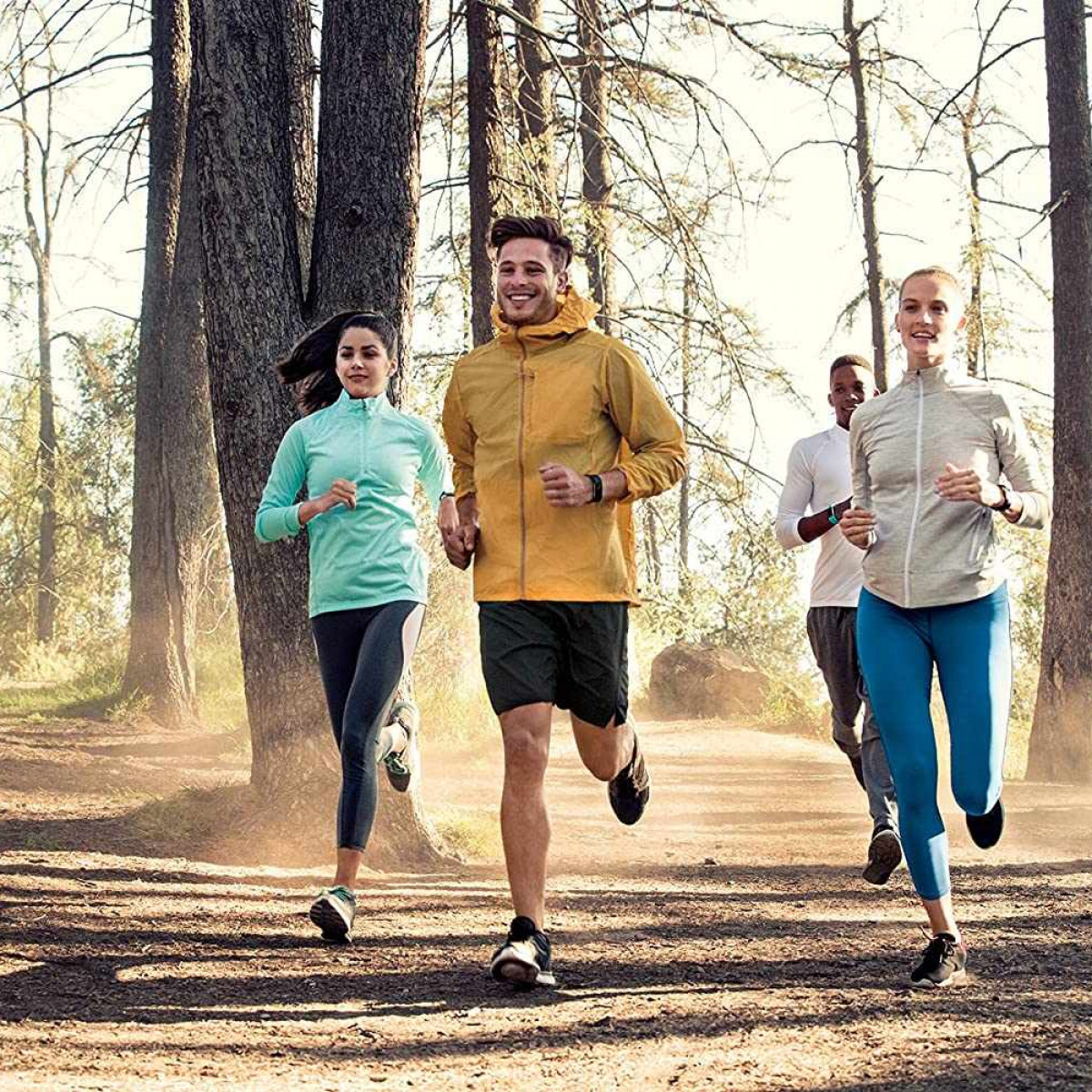 Cuatro personas corriendo por un camino de tierra en un bosque.