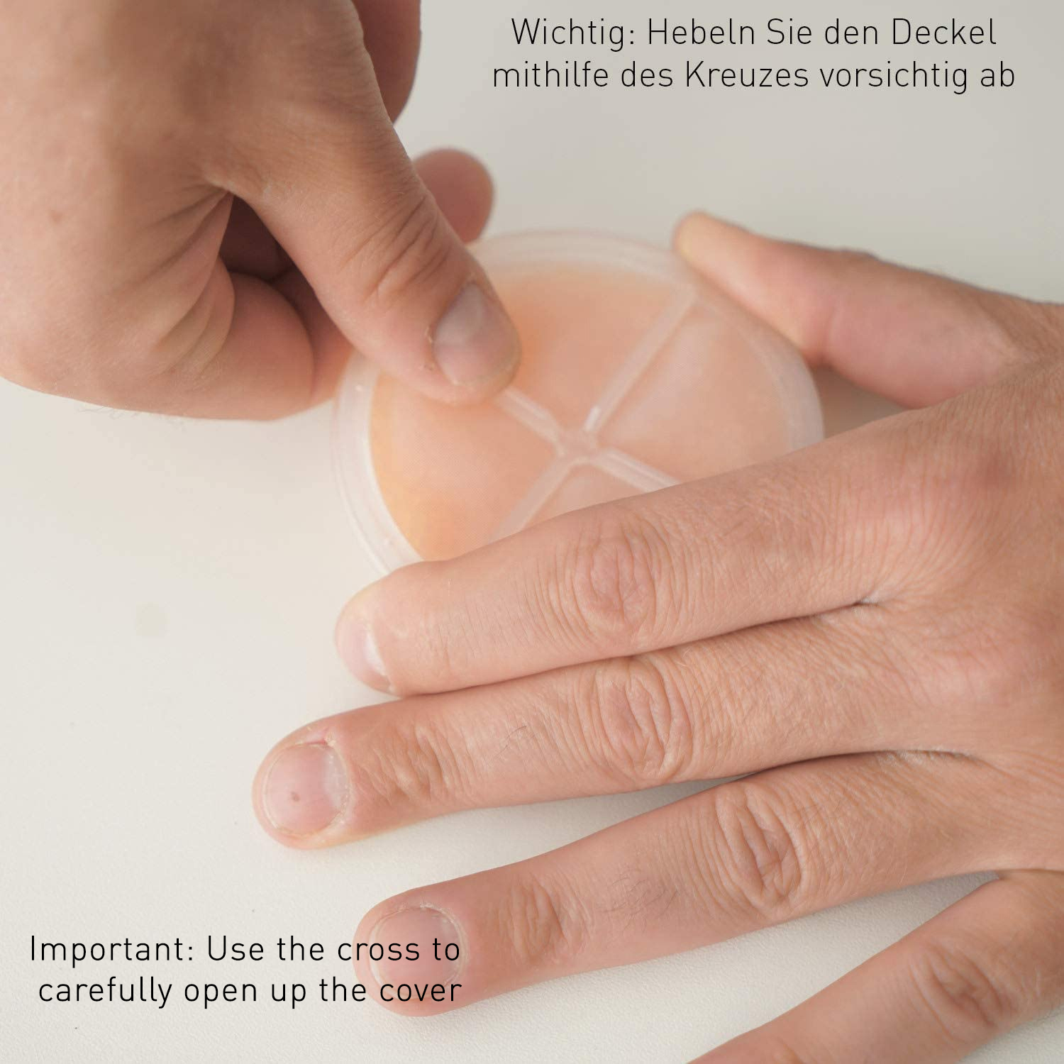 Zwei Hände öffnen vorsichtig einen runden, pfirsichfarbenen Behälter, der Deckel wird von den Fingern gehalten.