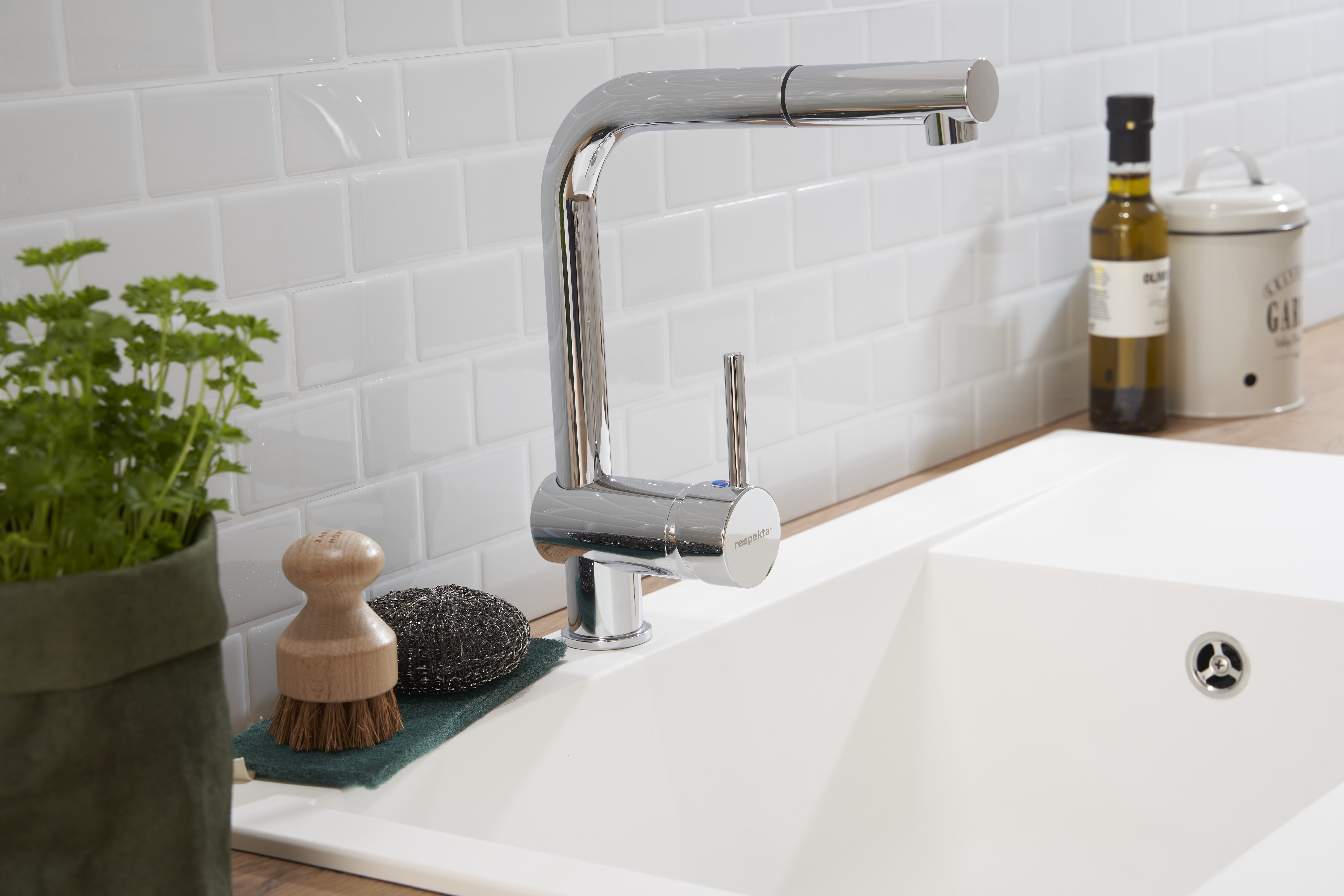 Weißes Küchenwaschbecken mit Wasserhahn, Spülbürste und Seife. Weiße Fliesenspiegel und Holztheke.