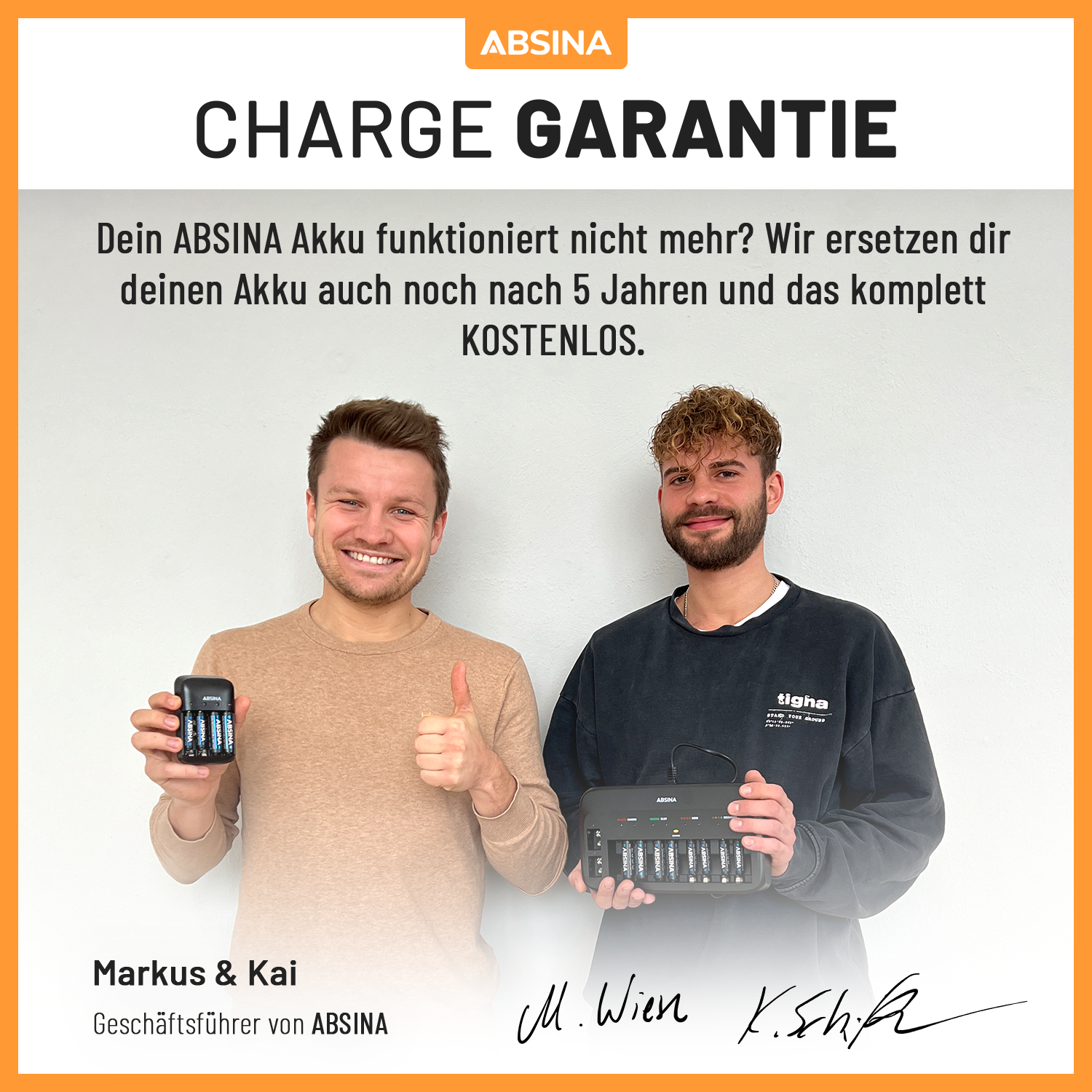 Zwei Männer halten Batterien und ein Ladegerät, lächeln.