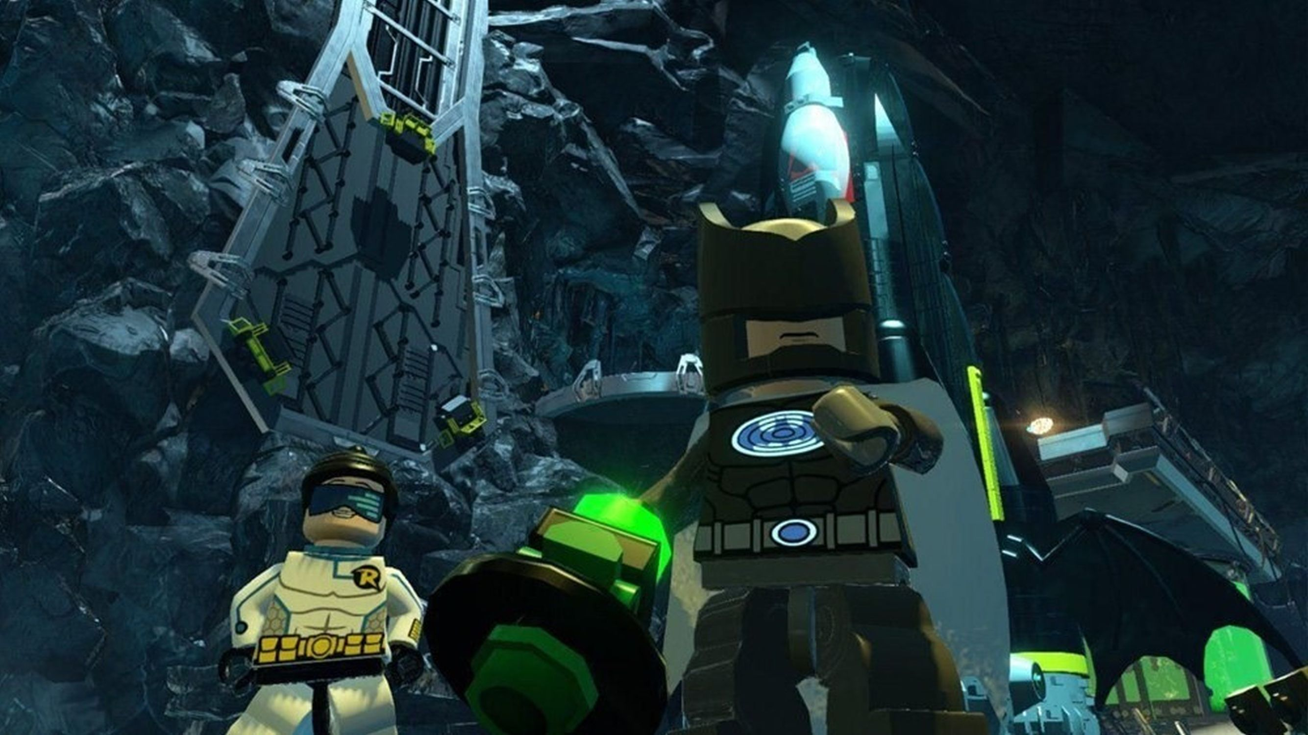 Figurines Lego Batman et Robin dans une grotte sombre, avec un objet vert.
