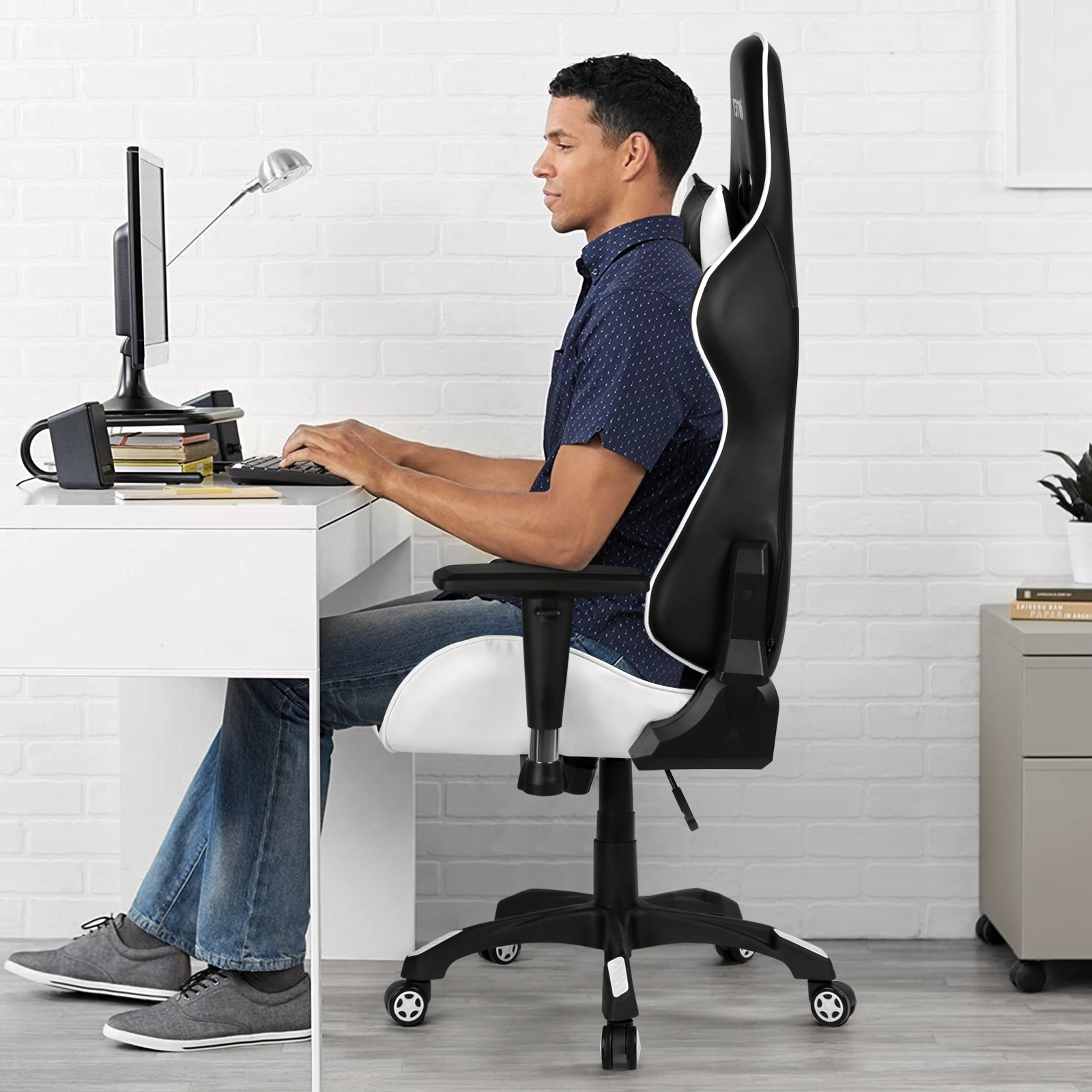 Ein Mann sitzt an einem Schreibtisch und benutzt einen Computer, in einem schwarz-weißen Gaming-Stuhl.