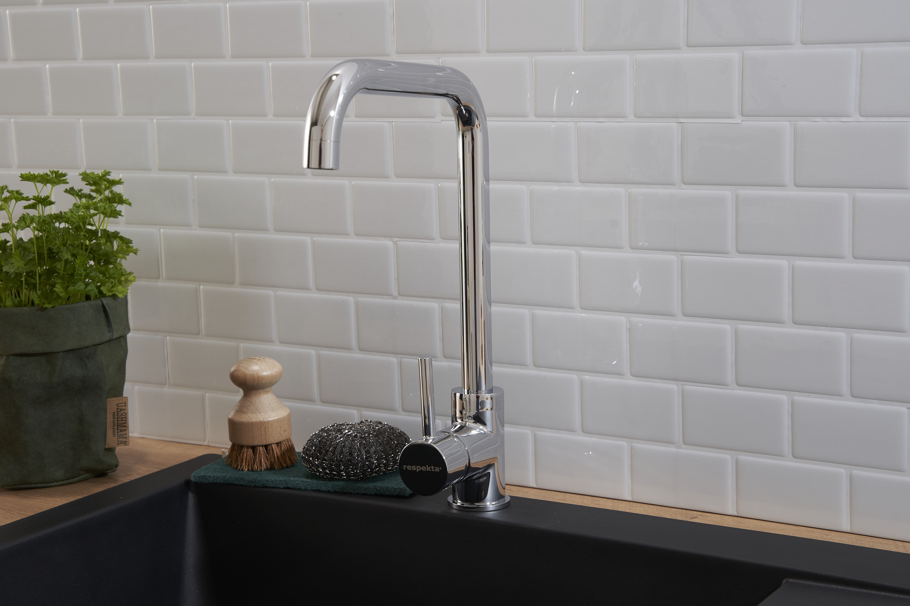 Chrom-Wasserhahn über einem schwarzen Waschbecken, weiß geflieste Wand im Hintergrund.