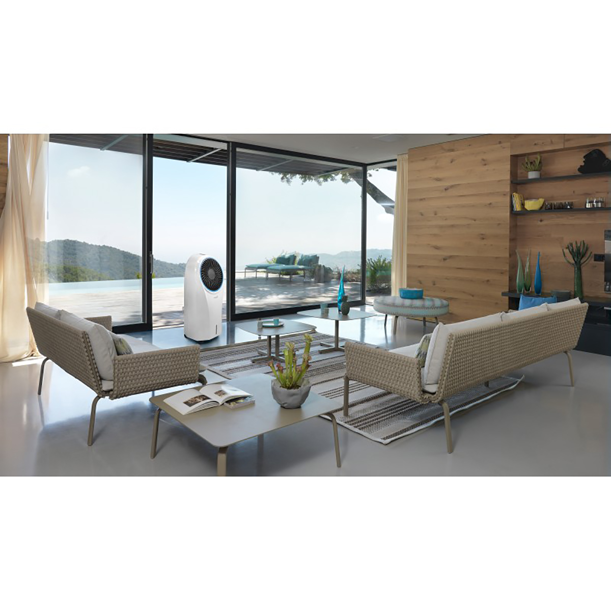 Salón con sillas, enfriador de aire y vista panorámica. Fondo: montañas y cielo.