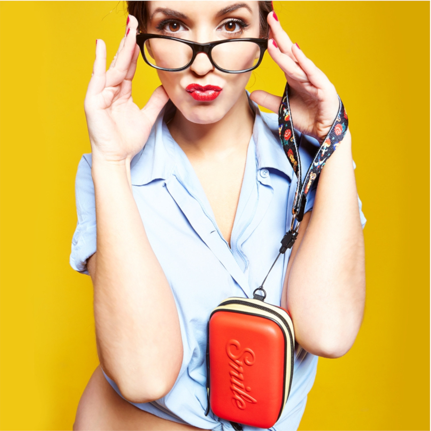 Frau mit Brille, rotem Lippenstift, gelbem Hintergrund und roter Tasche mit Riemen.