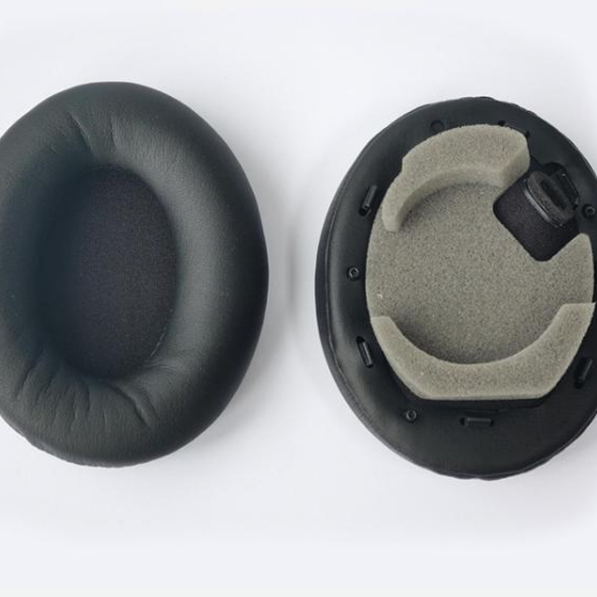 Dwie czarne poduszki do słuchawek, jedna z pianką, a druga bez.