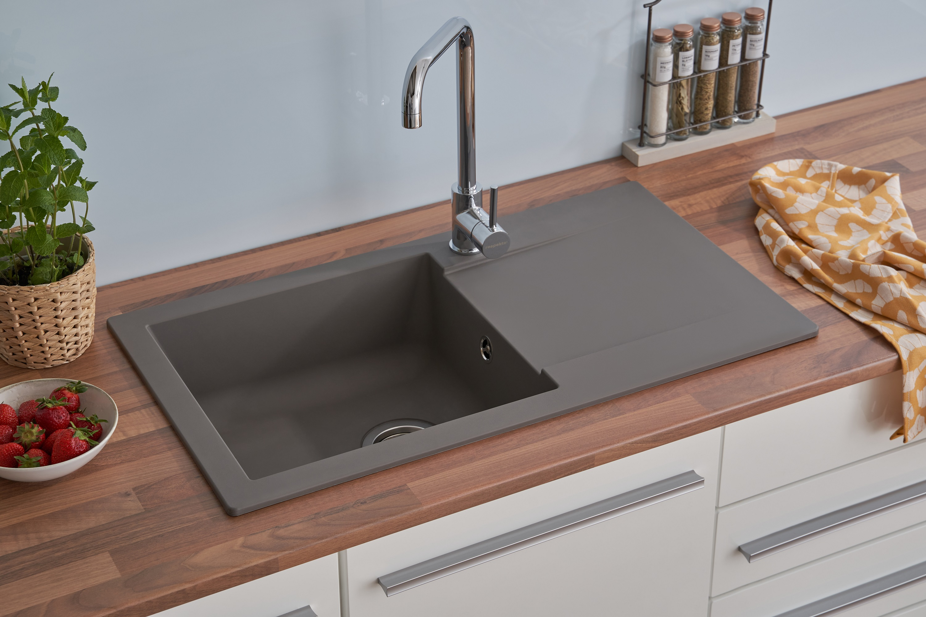 Küchenspüle mit Wasserhahn auf einer Holz-Arbeitsplatte. Weiße Schränke. Erdbeeren und ein Handtuch. Hellblaue Wand.