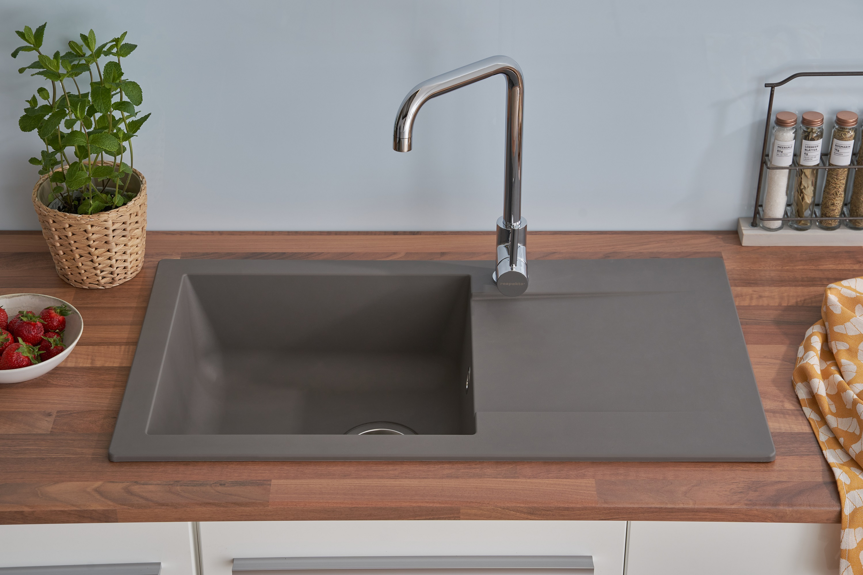 Ein Küchenspülbecken mit Wasserhahn auf einer Holz-Arbeitsplatte. Eine Schale mit Erdbeeren und Kräutern ist in der Nähe.