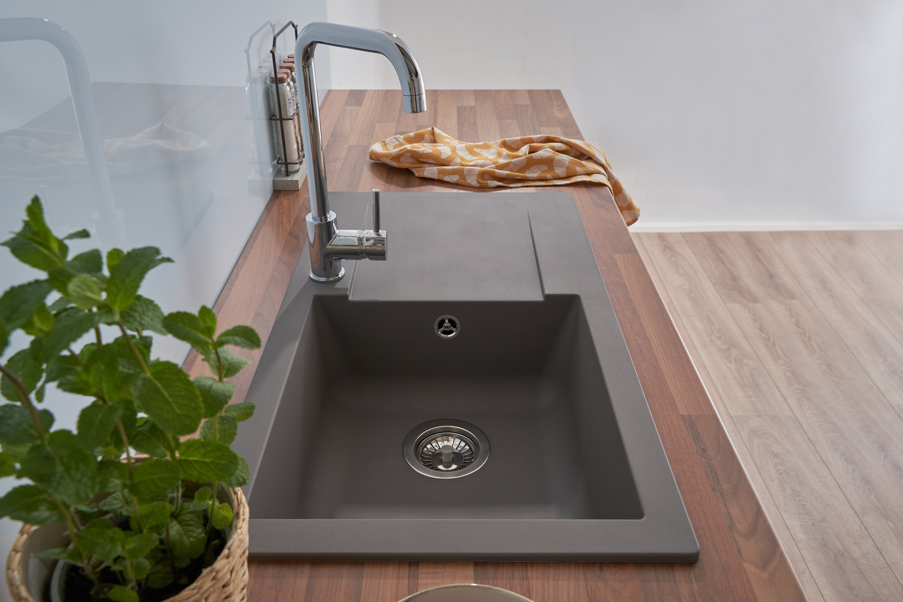 Ein graues Küchenbecken mit Wasserhahn, Holz-Arbeitsplatte und einer Pflanze im Korb.
