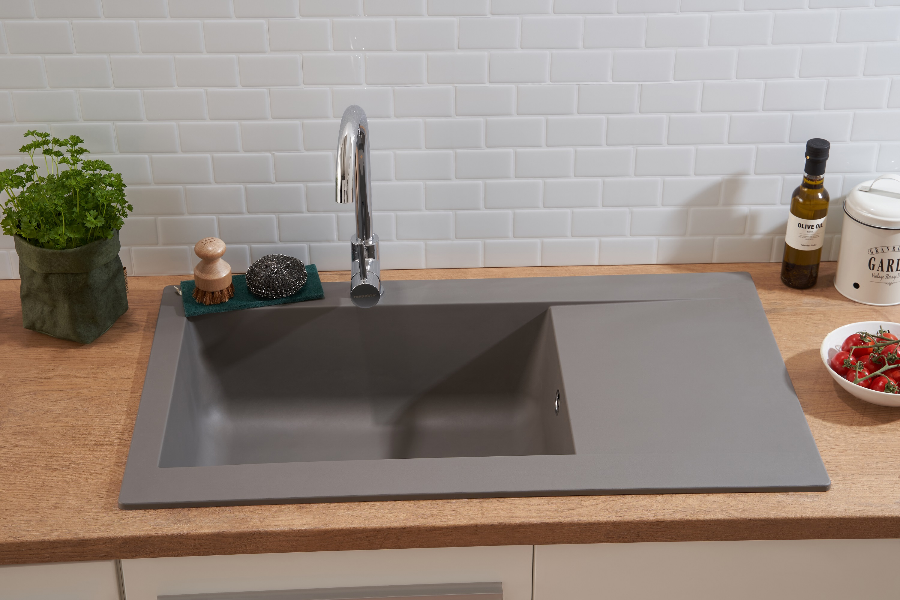 Ein graues Waschbecken mit Wasserhahn und Arbeitsplatte. Um das Waschbecken herum befinden sich Küchenutensilien.
