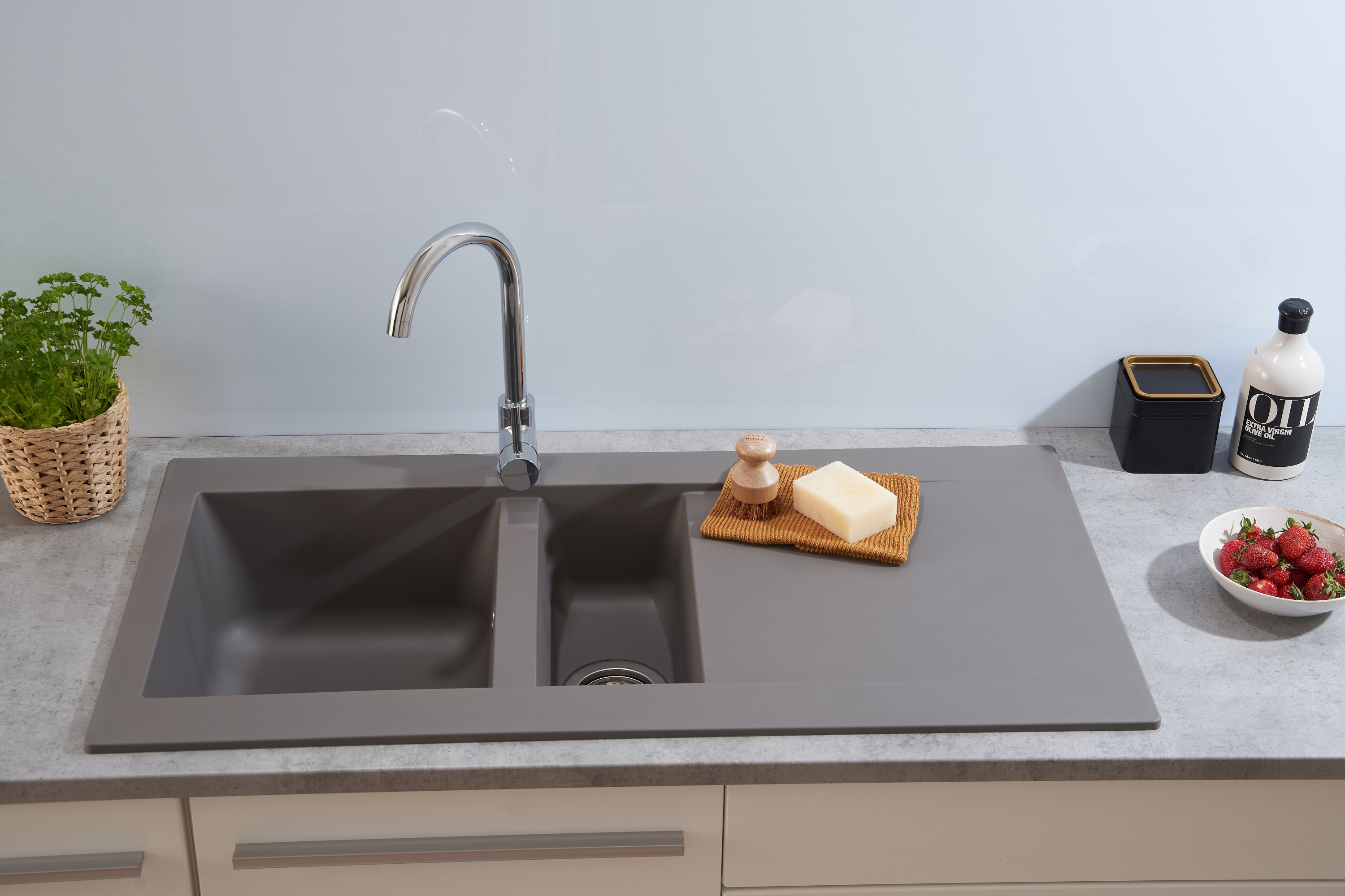 Ein graues Küchenbecken mit zwei Becken. Ein Wasserhahn befindet sich in der Mitte. Zubehör und Essen sind in der Nähe.