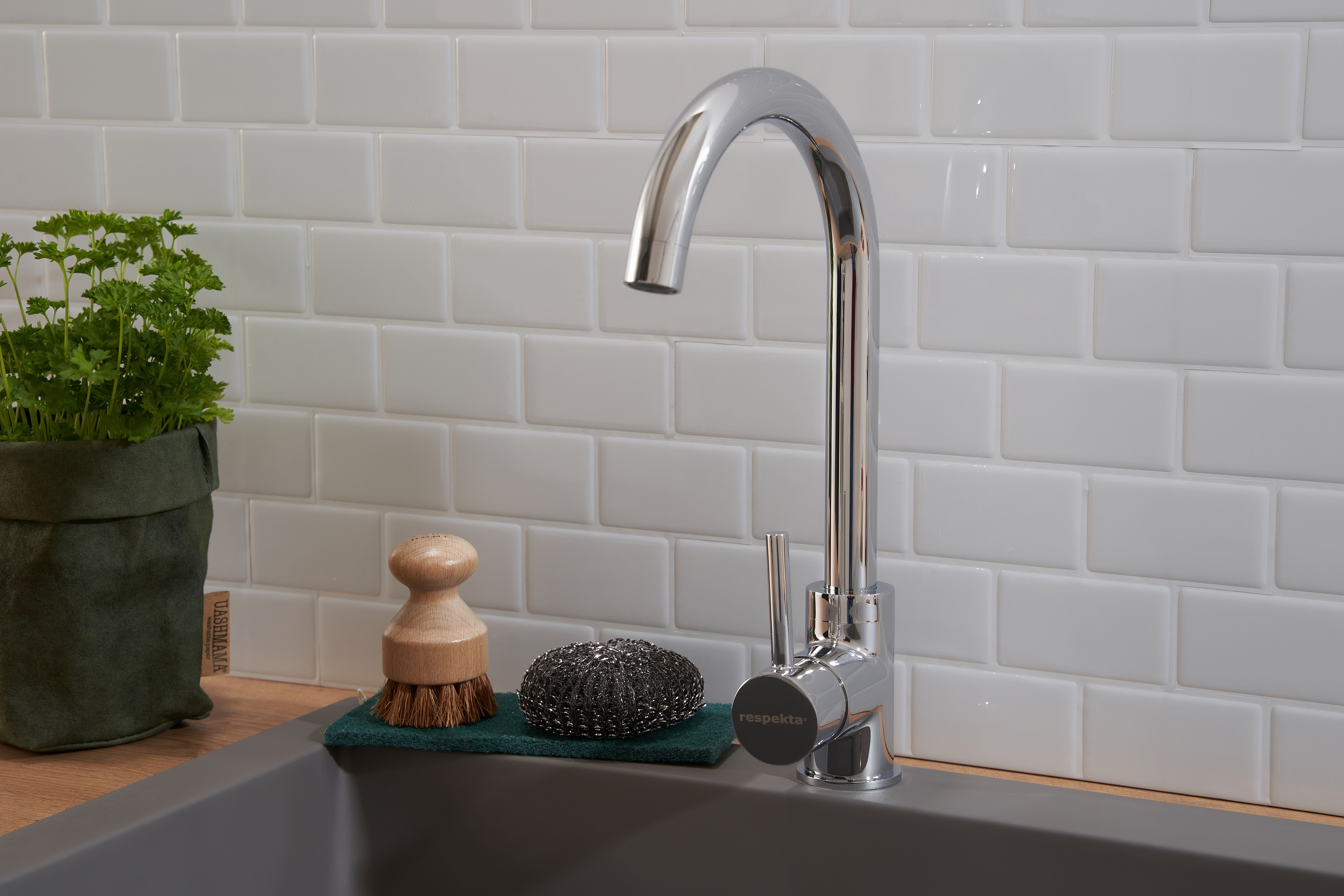 Chrom-Wasserhahn über einem grauen Waschbecken. Eine Bürste und ein Schwamm liegen im Becken.