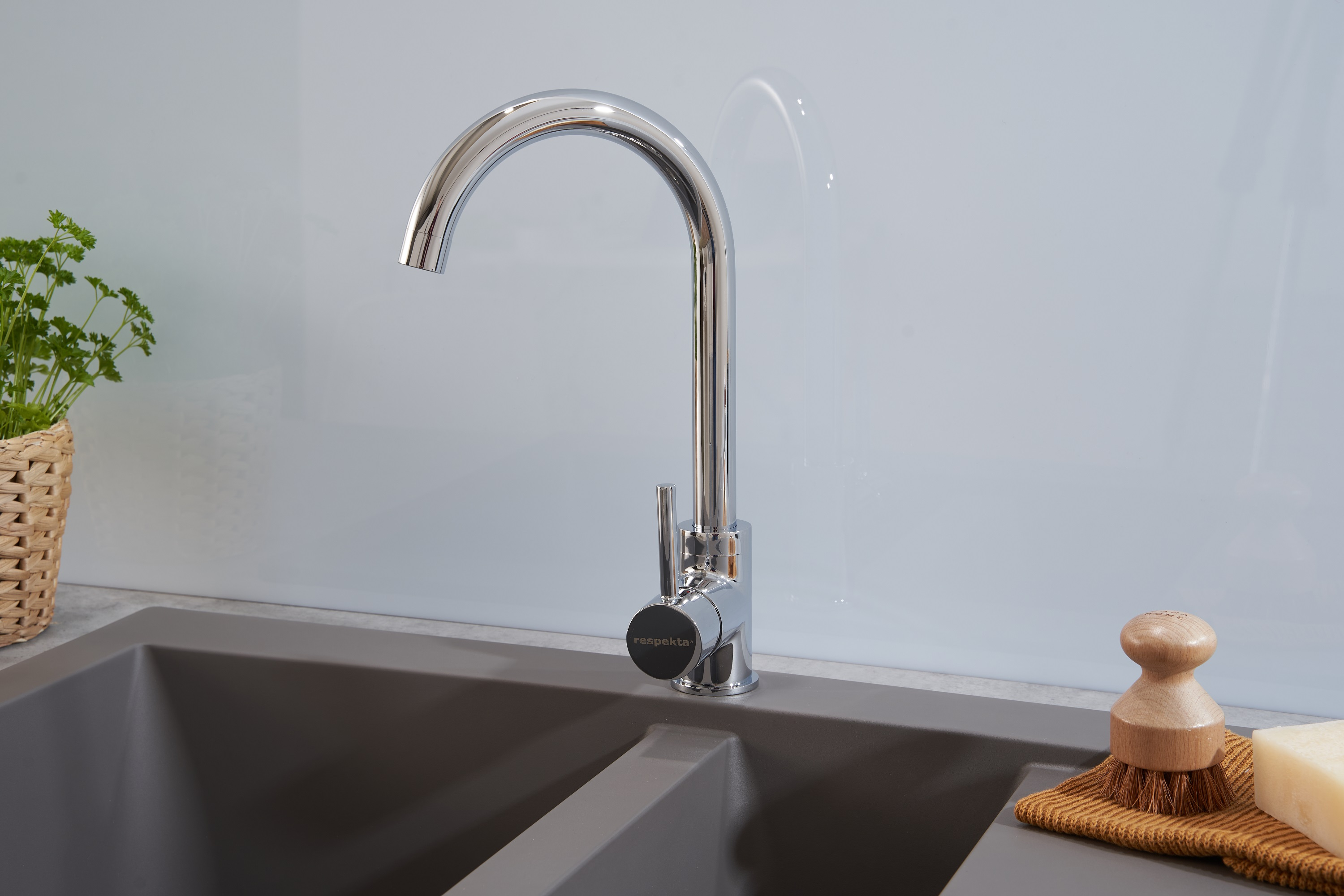 Chrom-Küchenarmatur über grauem Waschbecken mit Holz-Bürste und Seife.