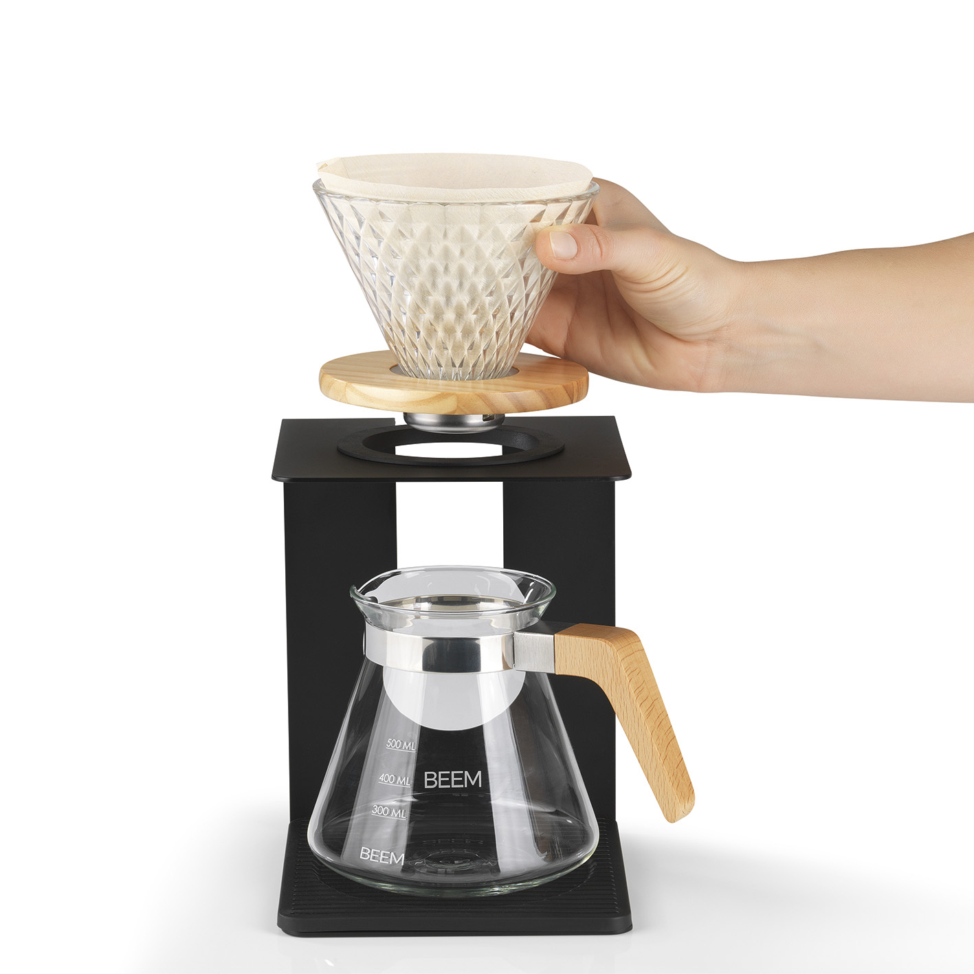 Eine Hand gießt Wasser in einen gläsernen Kaffeezubereiter. Das Set steht auf einem schwarzen Ständer.