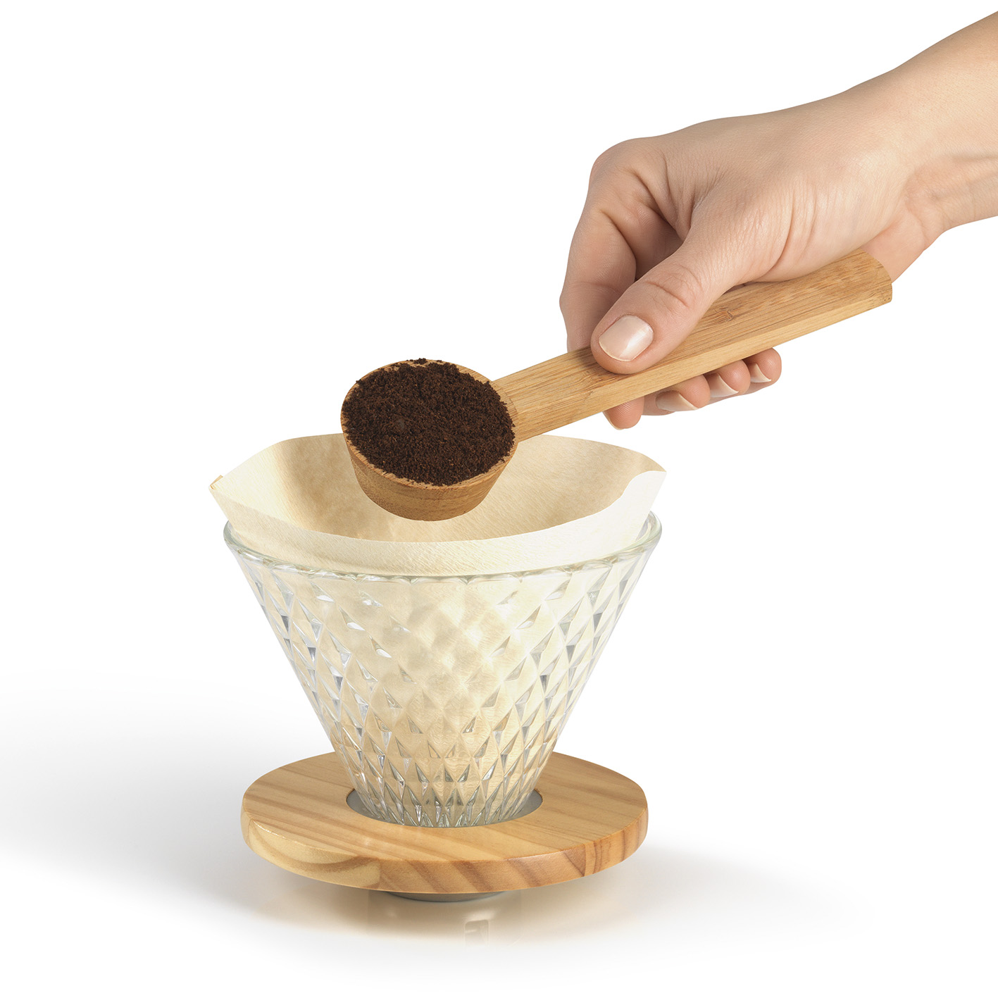 Eine Hand schüttet Kaffeepulver aus einem Holzschöpfer in einen Papierfilter in einem Glas-Kaffeebereiter.