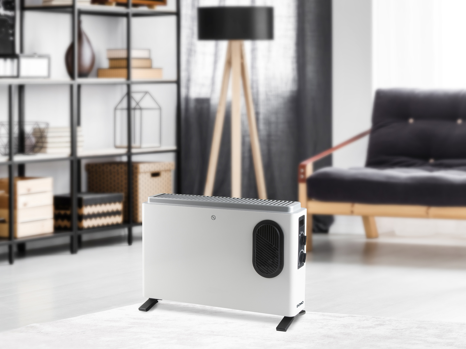 Biały grzejnik elektryczny z czarnym wentylatorem, na jasnym dywanie, z meblami w tle.