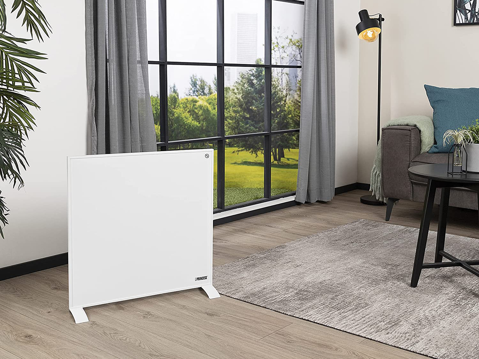 Witte elektrische kachel in een woonkamer. Het staat voor een raam met bomen zichtbaar buiten.