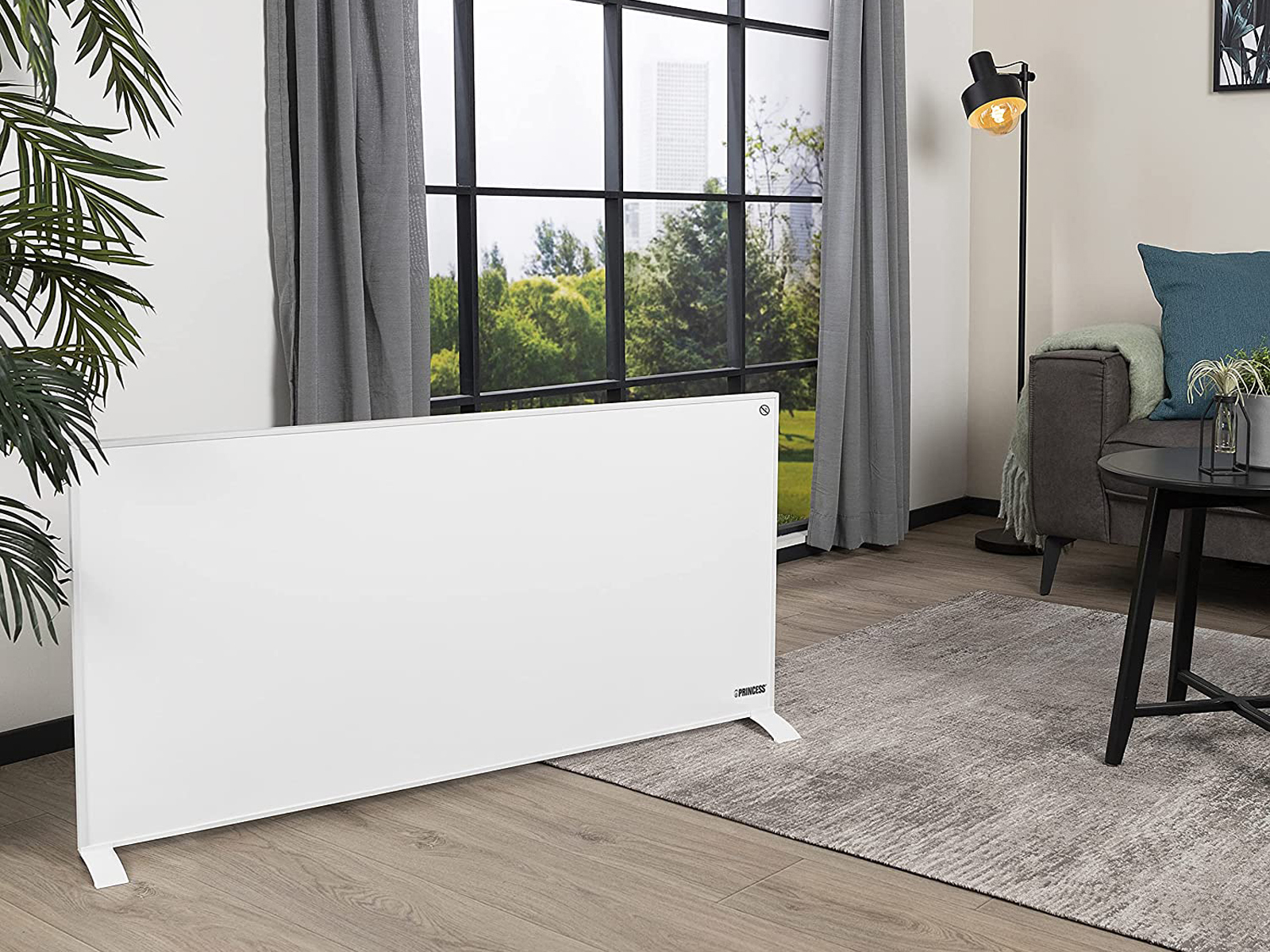 Ein weißer Heizkörper steht in einem Wohnzimmer, in der Nähe eines Fensters und einer Couch.