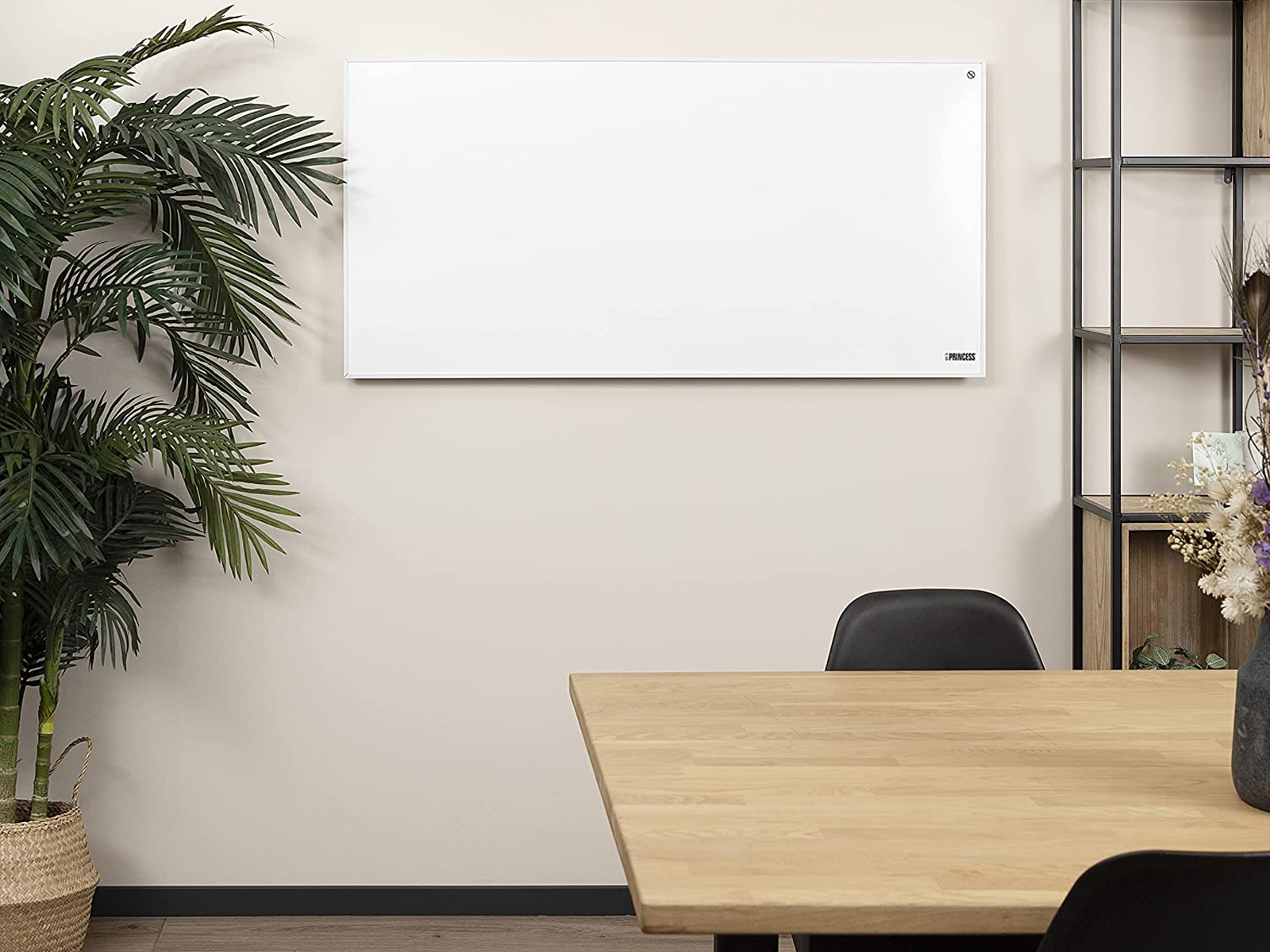Ein weißer, an der Wand befestigter Heizkörper an einer beigefarbenen Wand, mit einem Holztisch und einer Pflanze im Vordergrund.