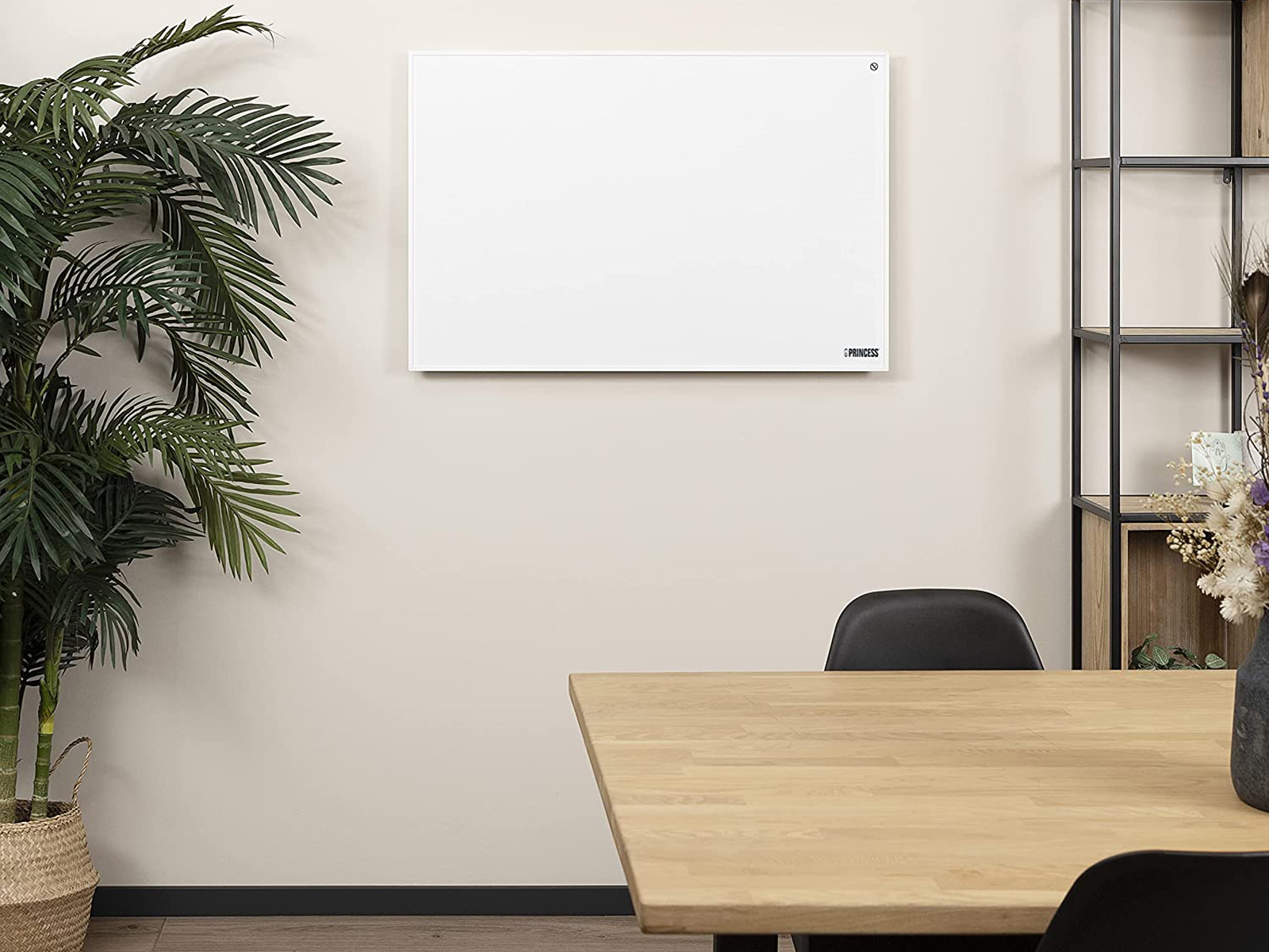 Een witte, rechthoekige verwarming aan een lichtgekleurde muur. Een houten tafel en planten in de buurt.
