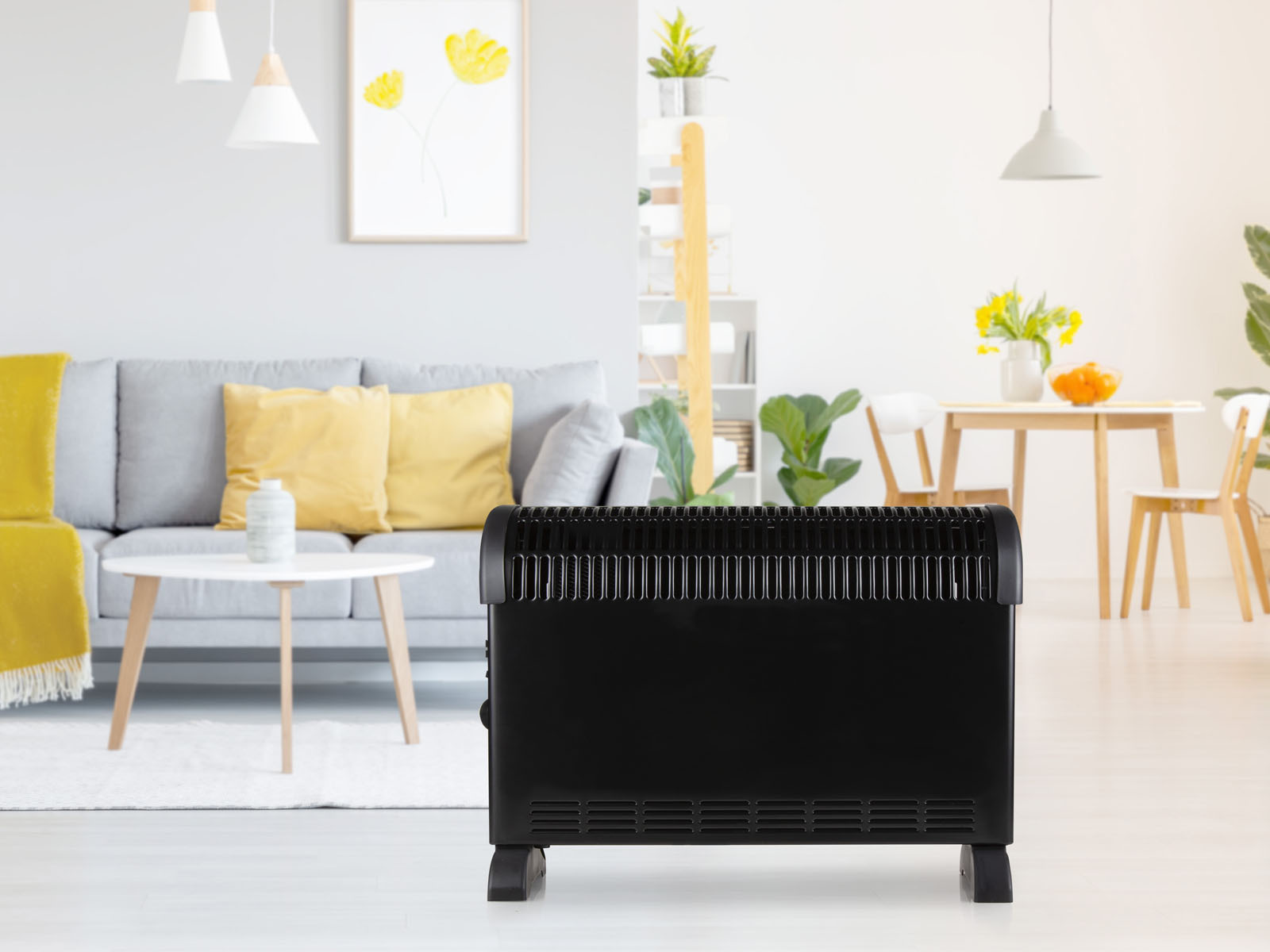 Schwarzer Elektroheizer in einem Wohnzimmer. Sofa, gelbe Kissen und Tisch sind im Hintergrund.