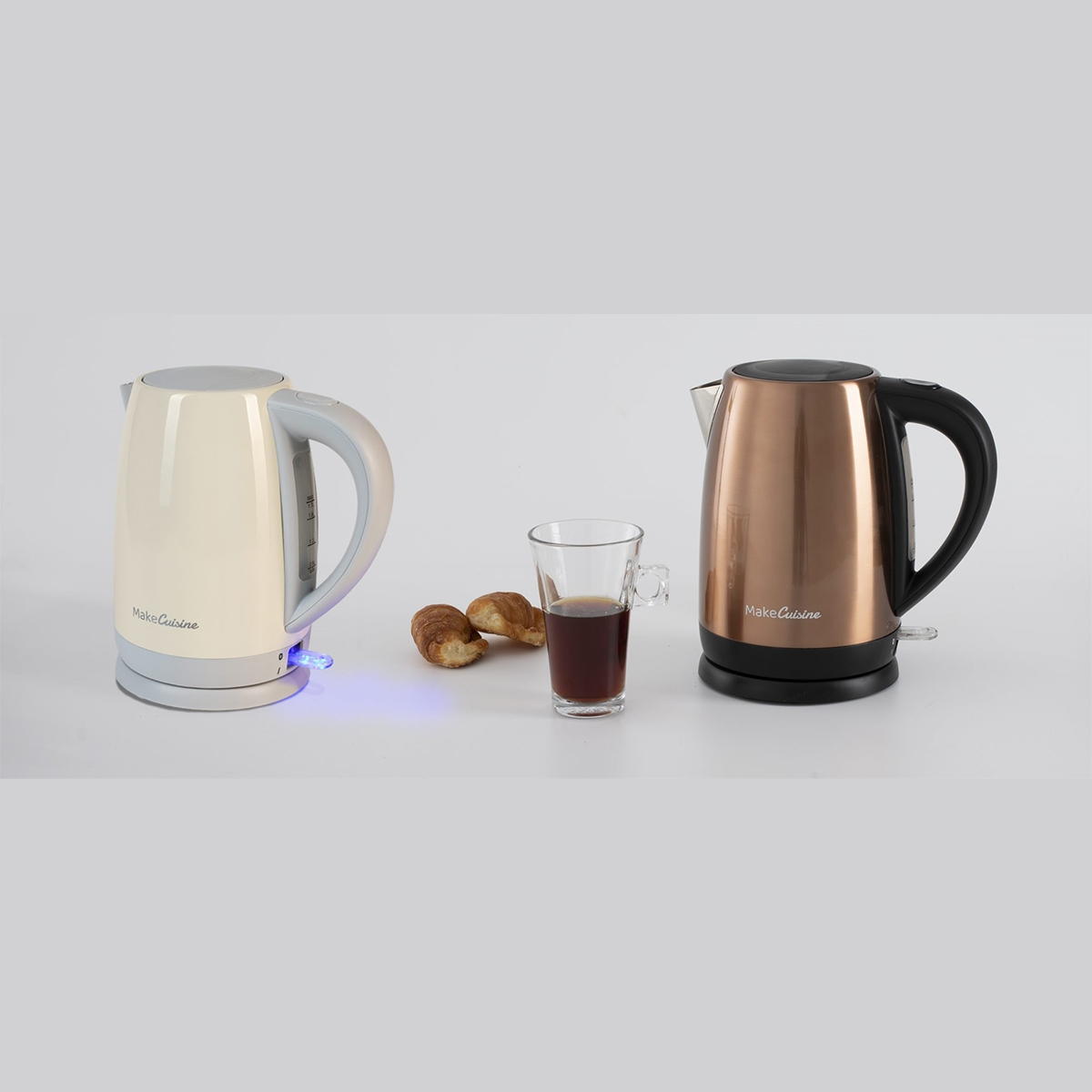 Dos hervidores eléctricos, café y cruasanes. Uno beige, uno cobrizo y un vaso con café.