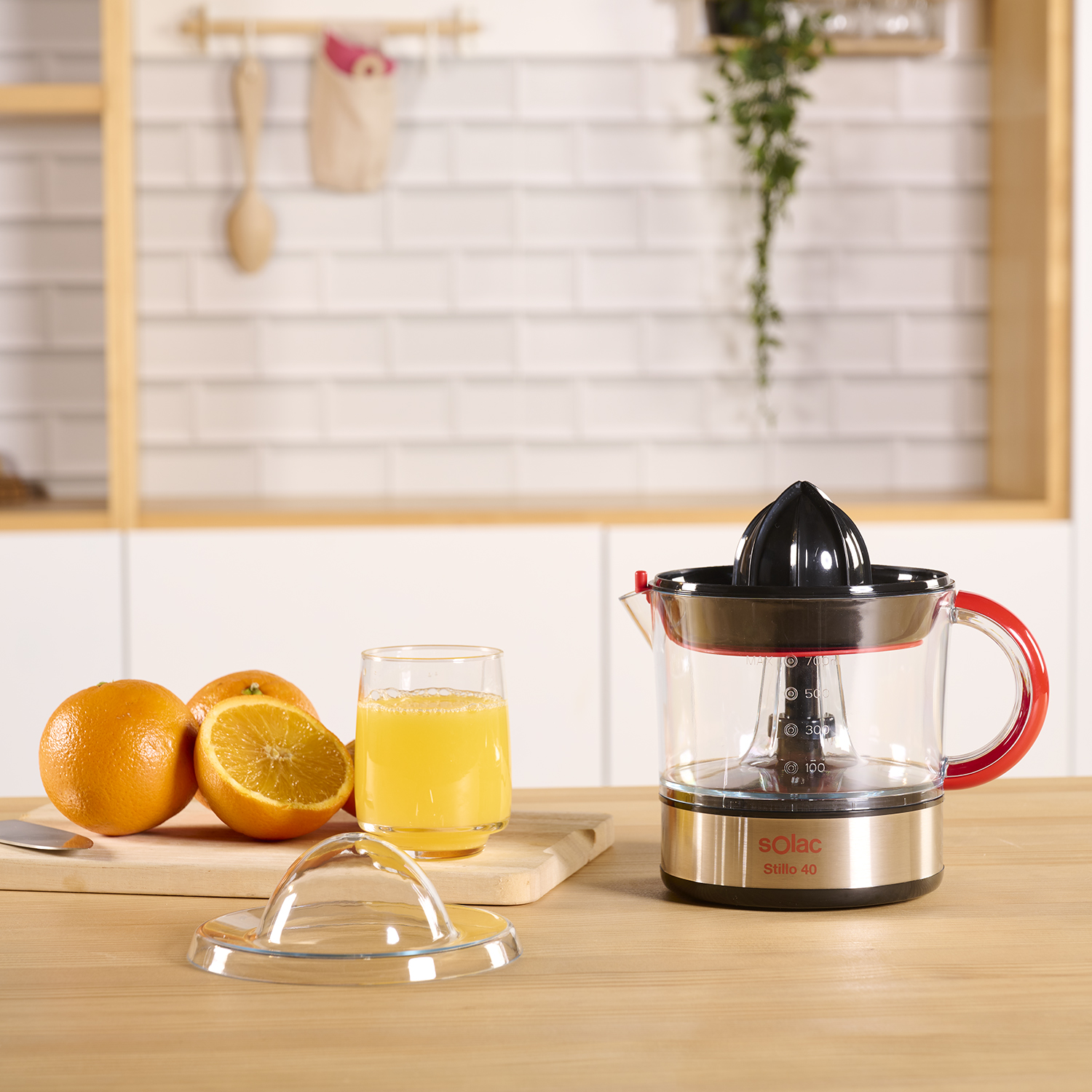 Naranjas, jugo y un exprimidor sobre una superficie de madera. Hay un vaso y una tabla de cortar.