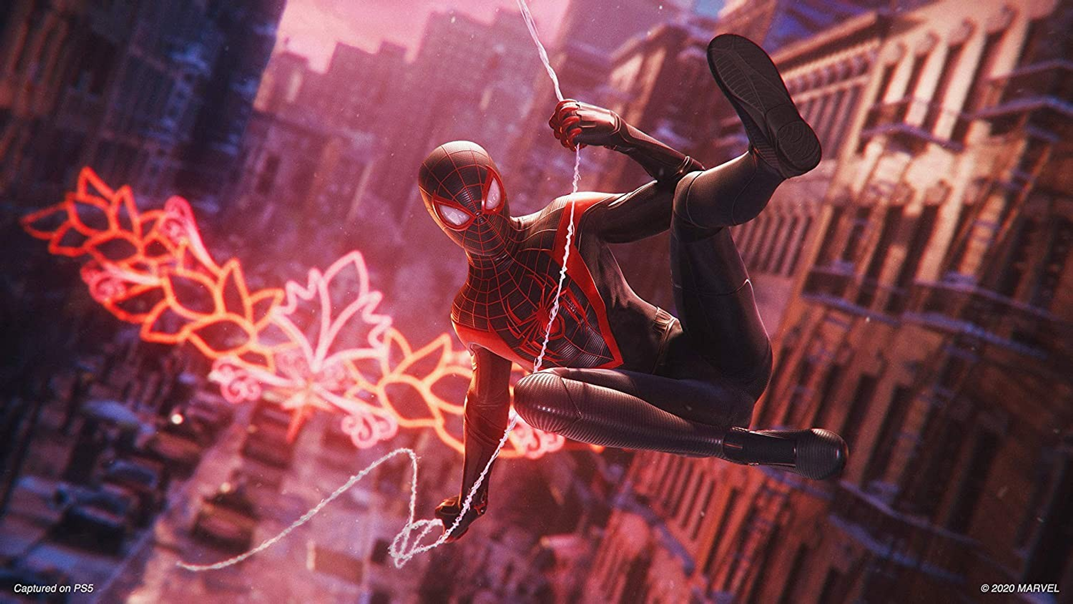 Spiderman w czarno-czerwonym kostiumie huśta się na pajęczynie w mieście.