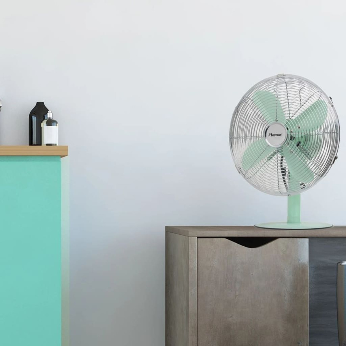 Ventilatore verde menta e argento su un mobile in legno, con un muro bianco sullo sfondo.