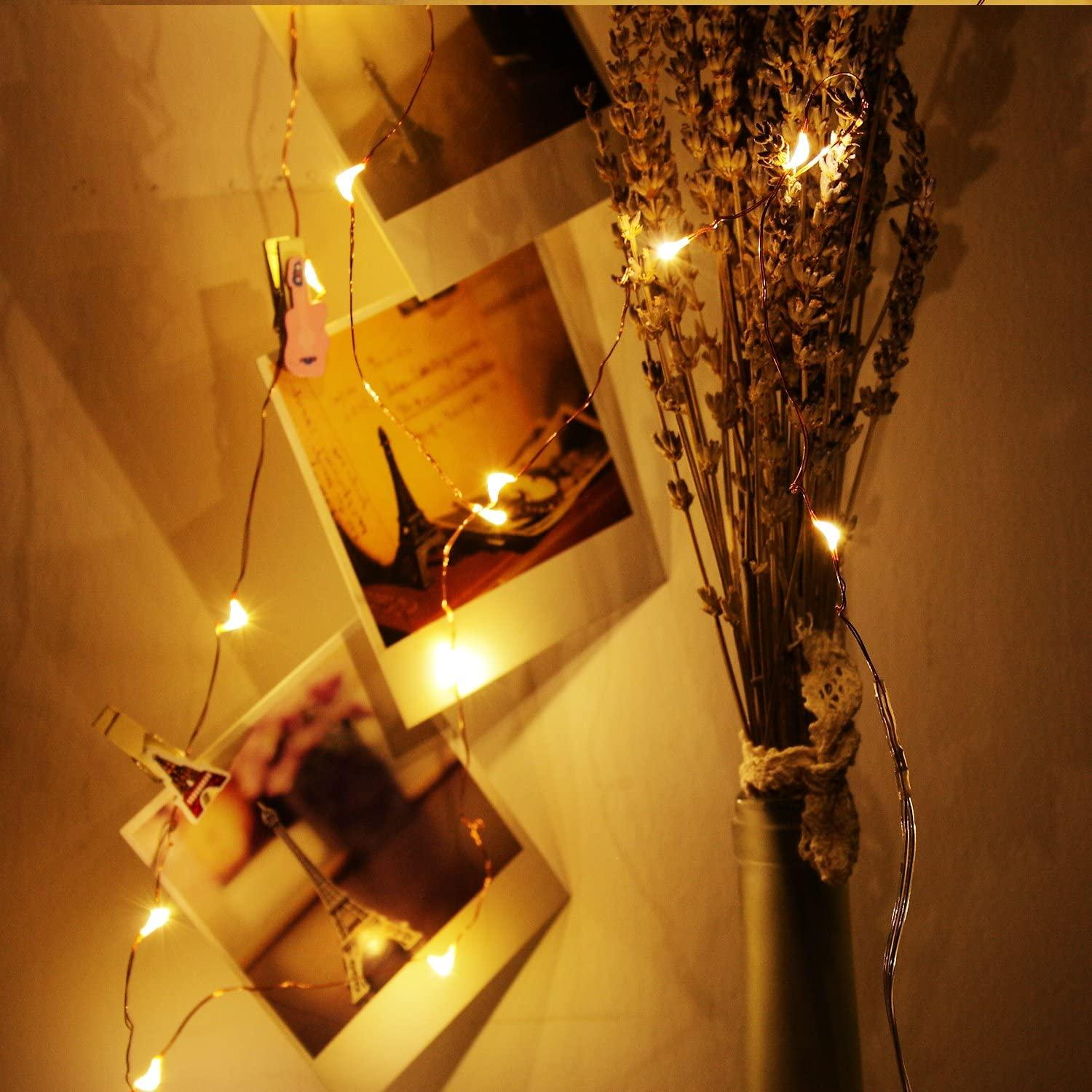 Zdjęcia na ścianie ze światłami i wazonem z suszonymi kwiatami, tworzące ciepłą, przytulną atmosferę.