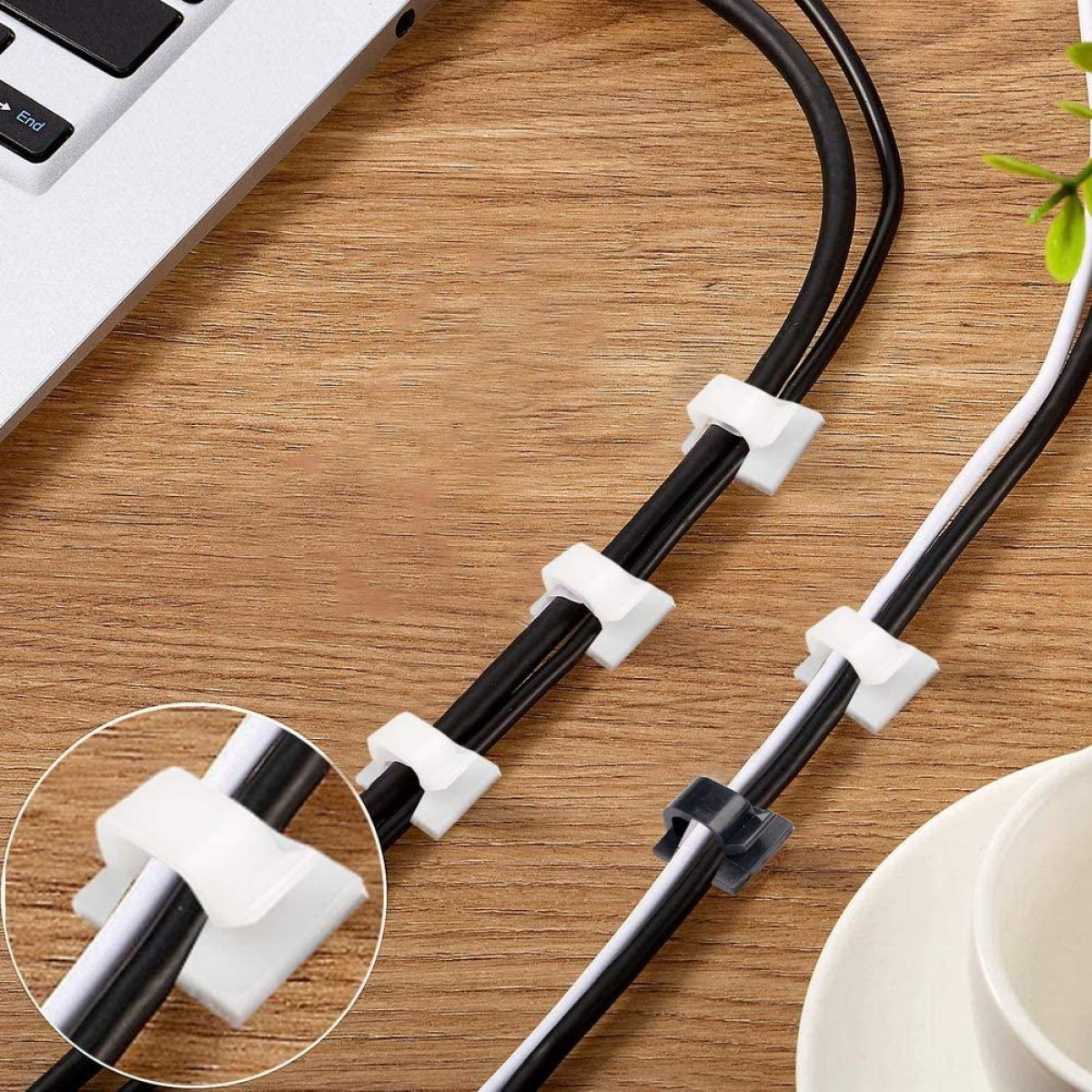 Kabel, die von weißen und schwarzen Kabelclips gehalten werden. Ein Laptop und eine weiße Tasse im Hintergrund.