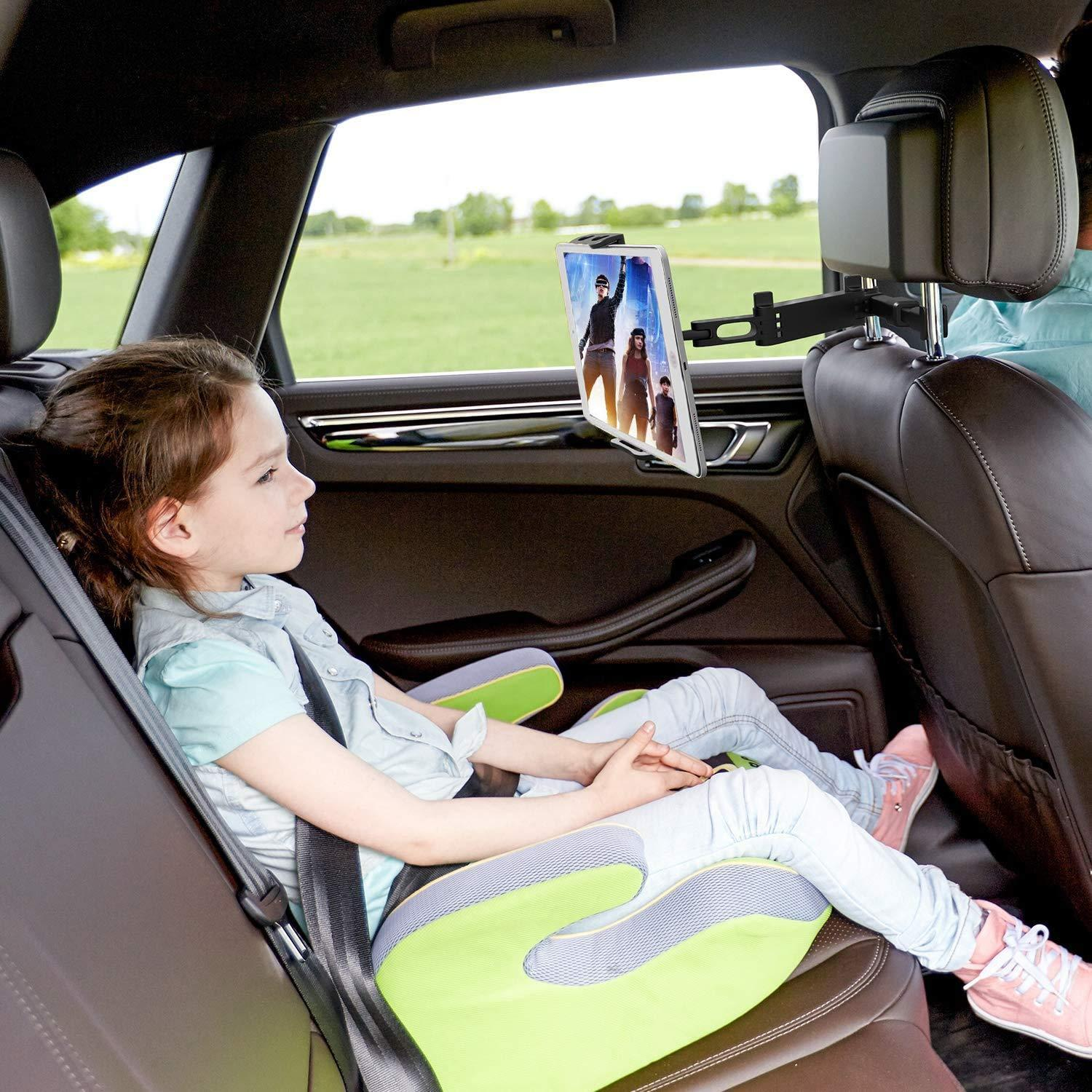 Mała dziewczynka w foteliku samochodowym ogląda tablet zamontowany z tyłu siedzenia.