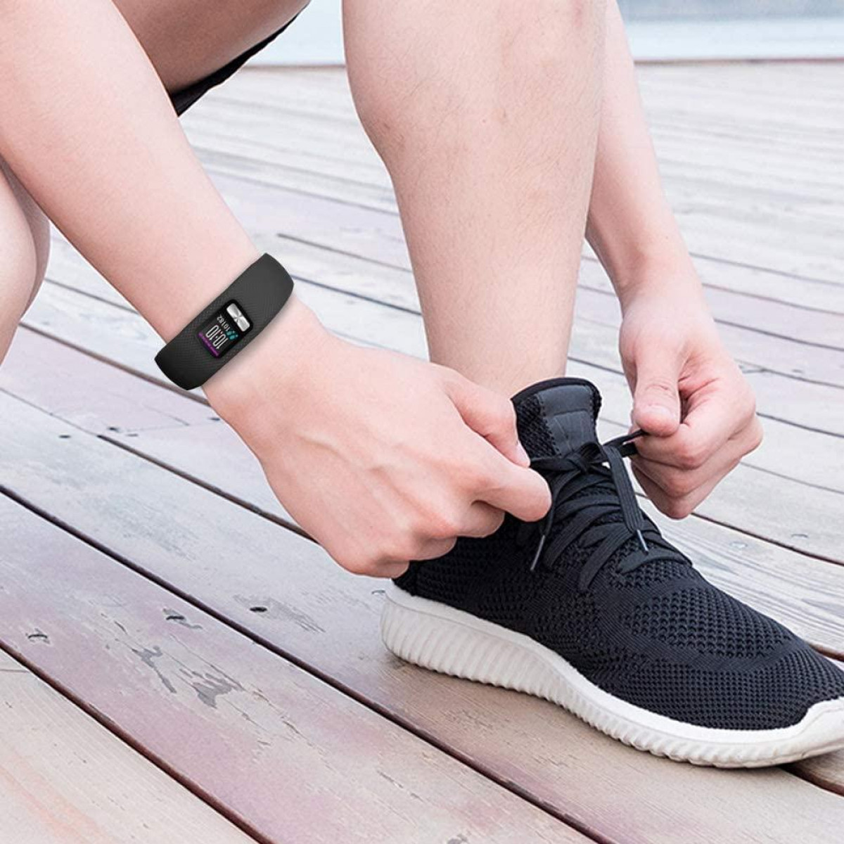 Osoba zawiązująca czarną sznurowadło, nosząca opaskę fitness na nadgarstku.