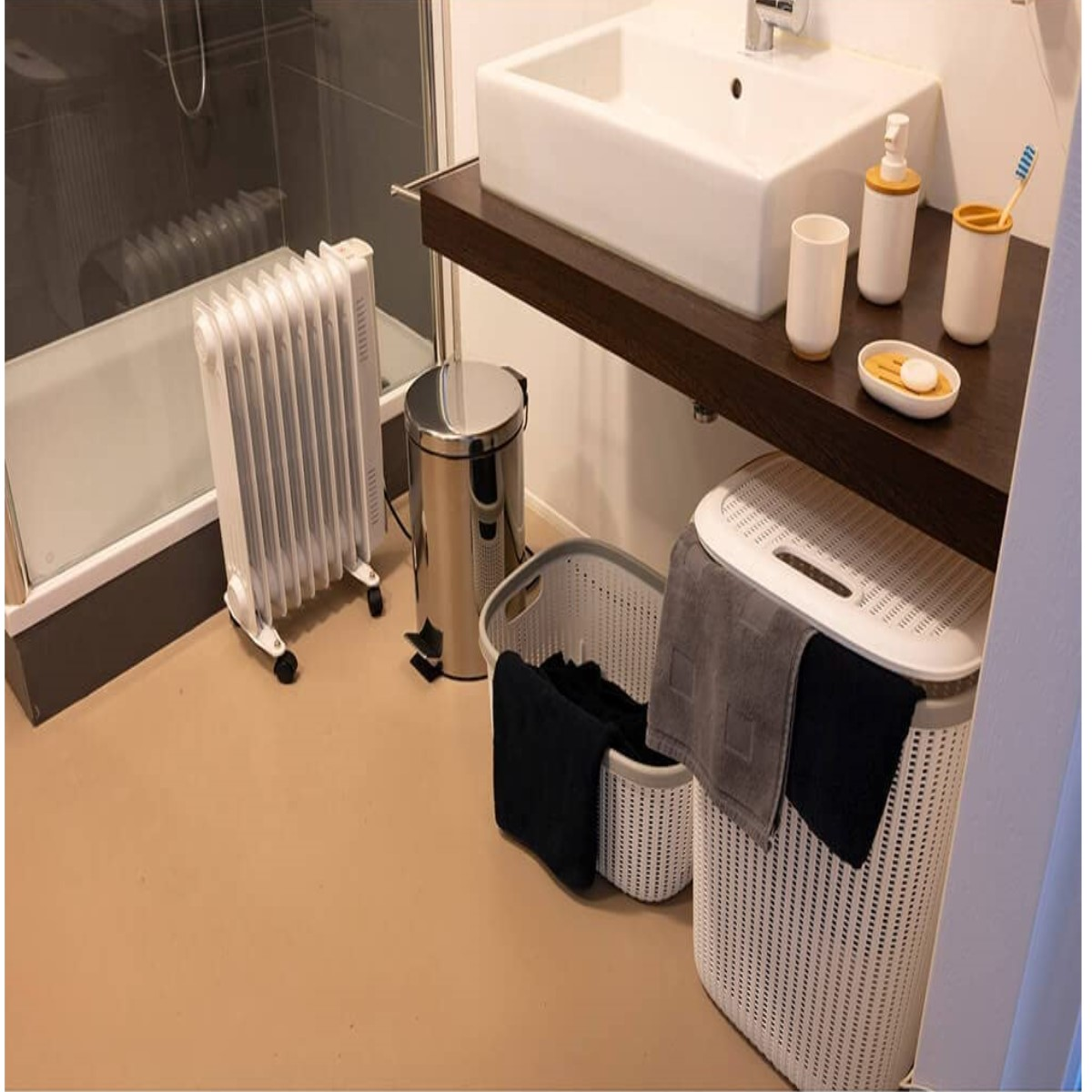 Badezimmerszene: ein weißes Waschbecken, Heizung, Mülleimer und Wäschekörbe mit Handtüchern und Toilettenartikeln.