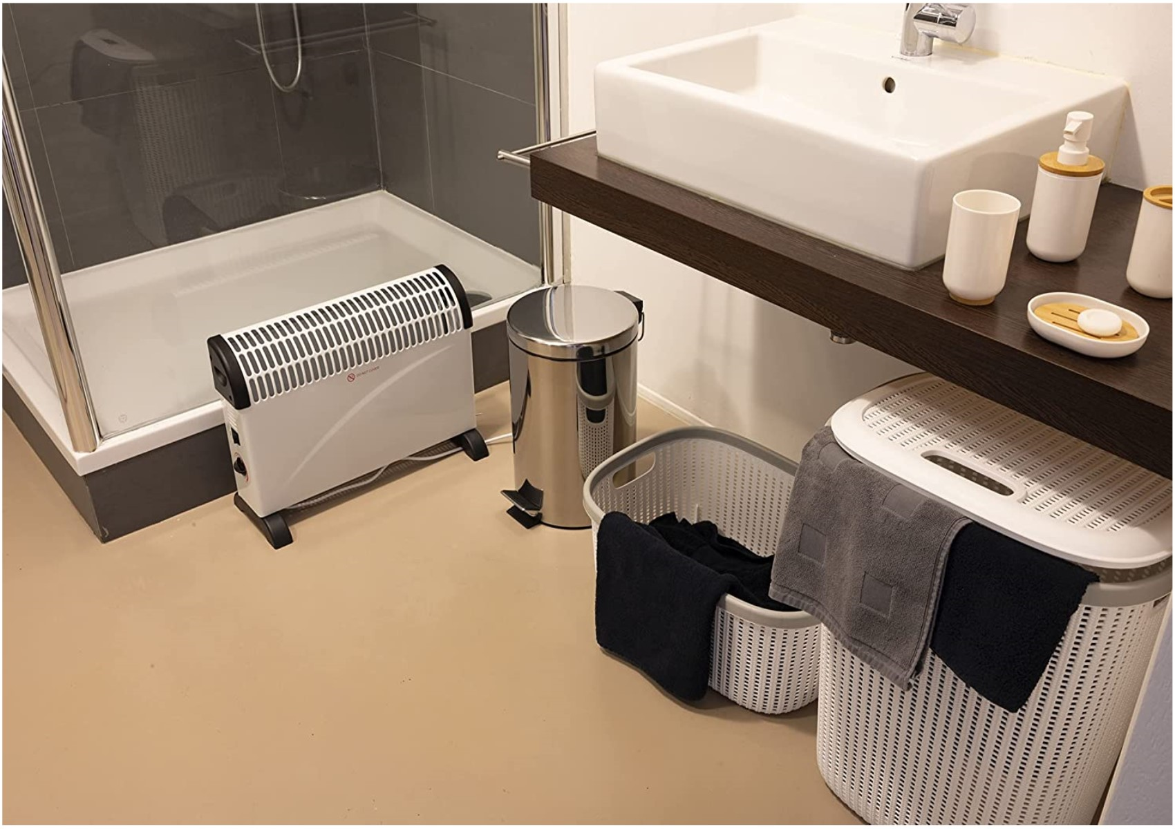 Ein Badezimmer mit Heizung, Waschbecken, Wäschekörben und Dusche. Der Raum hat hellen Bodenbelag.
