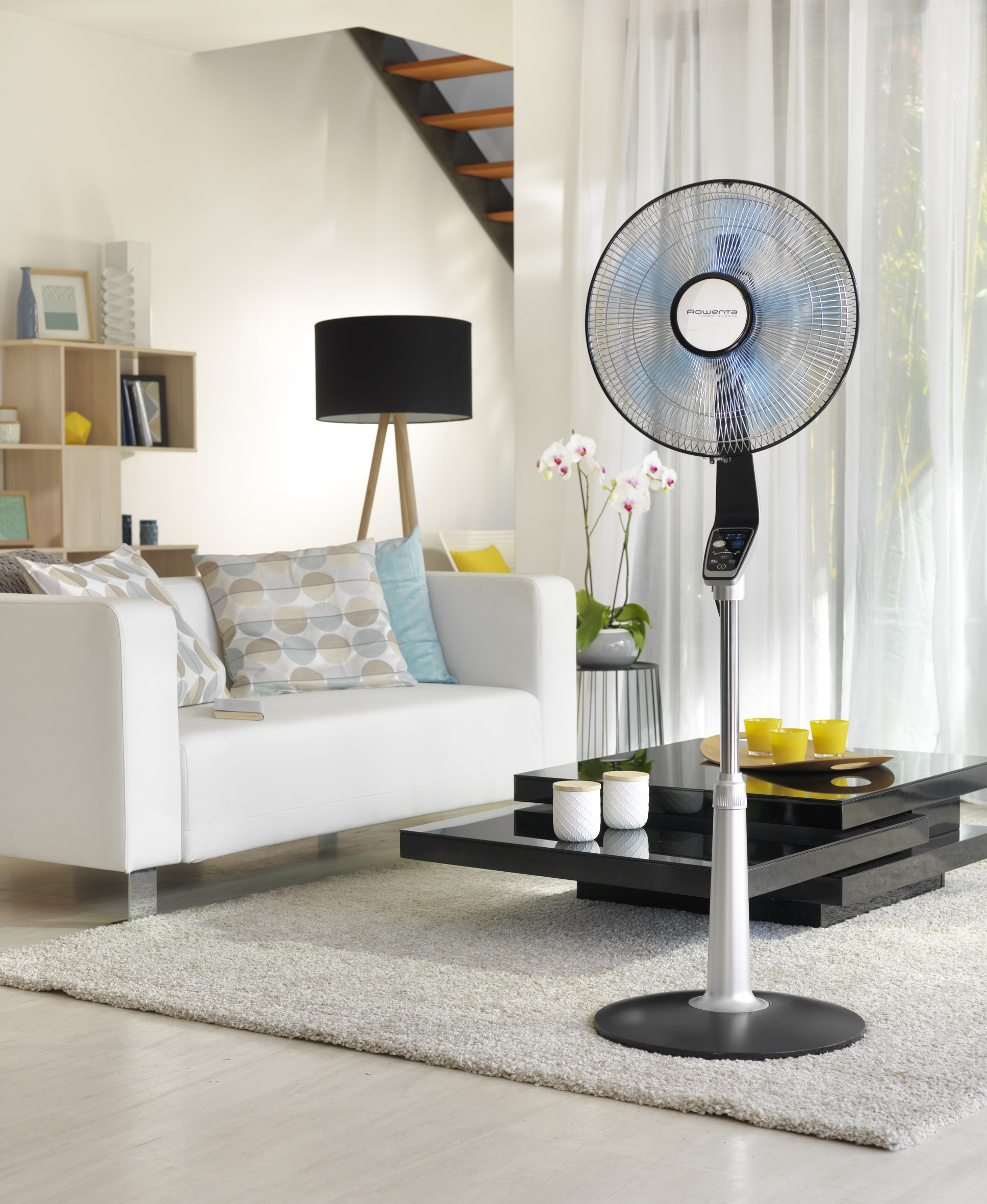 Wentylator stojący z niebieskimi łopatkami, biało-czarnym korpusem, w salonie.