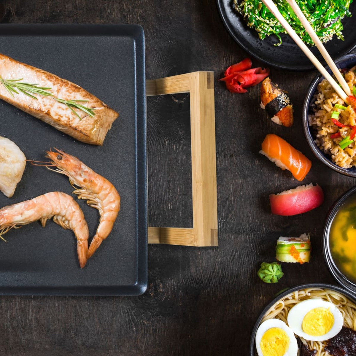 Sushi, gamberi, pesce e verdure su un tavolo di legno con bacchette.