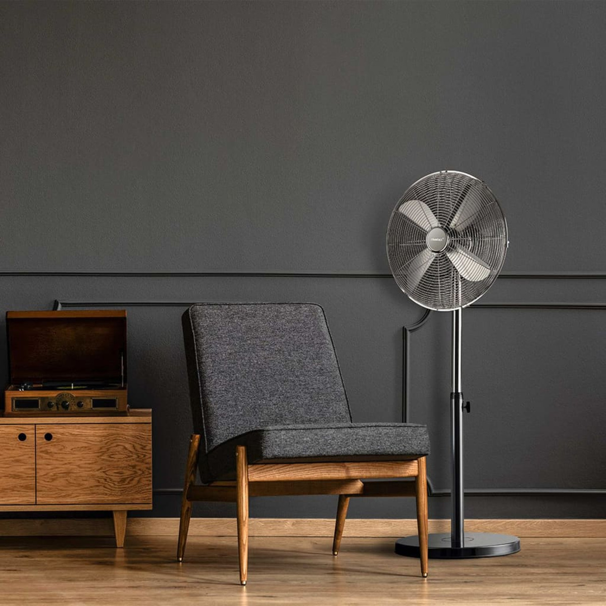 Una habitación moderna con ventilador, silla, tocadiscos y paredes gris oscuro.
