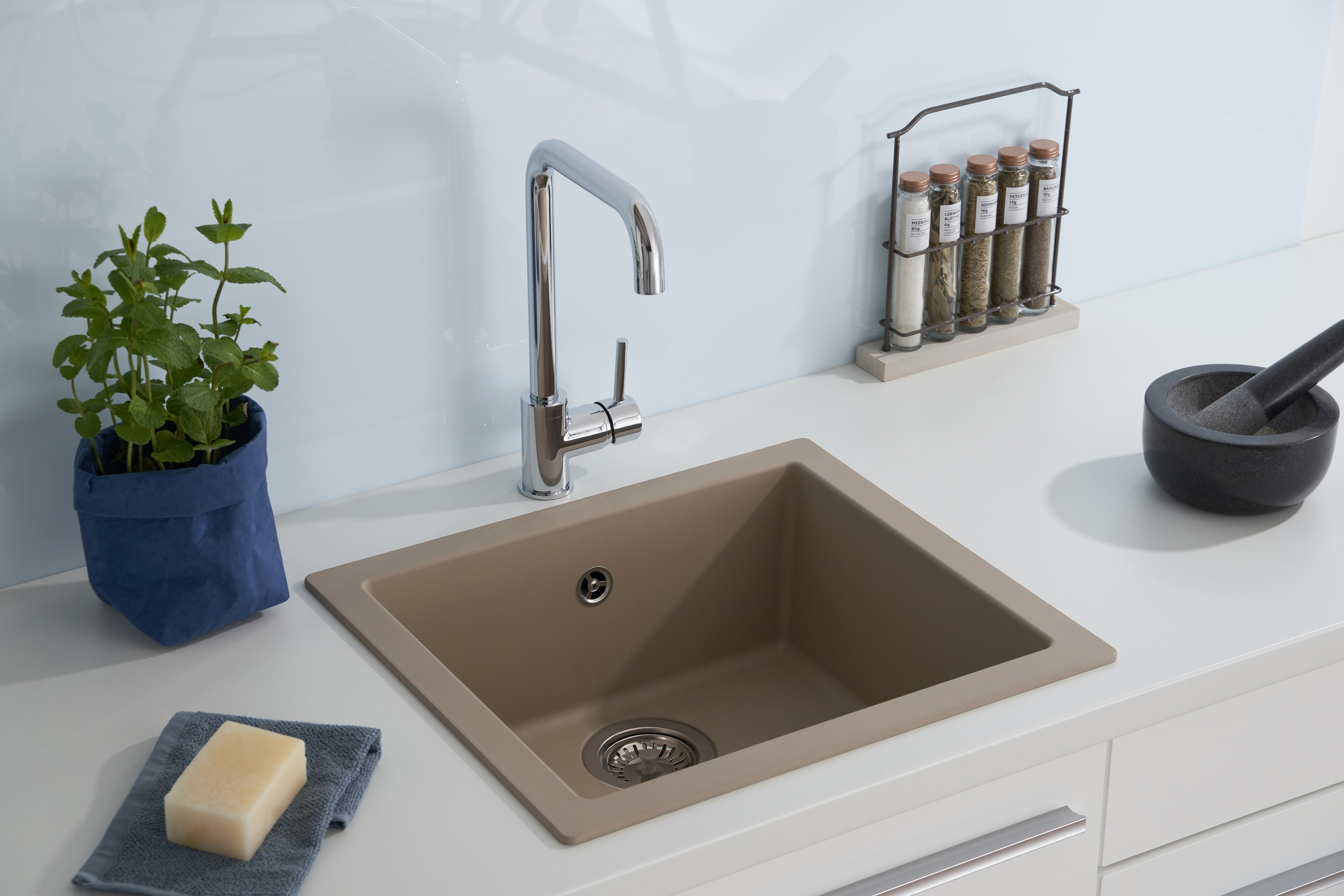 Küchenspüle mit Wasserhahn, Seife, Kräutern und einem Gewürzregal im Hintergrund. Das Waschbecken ist beige.
