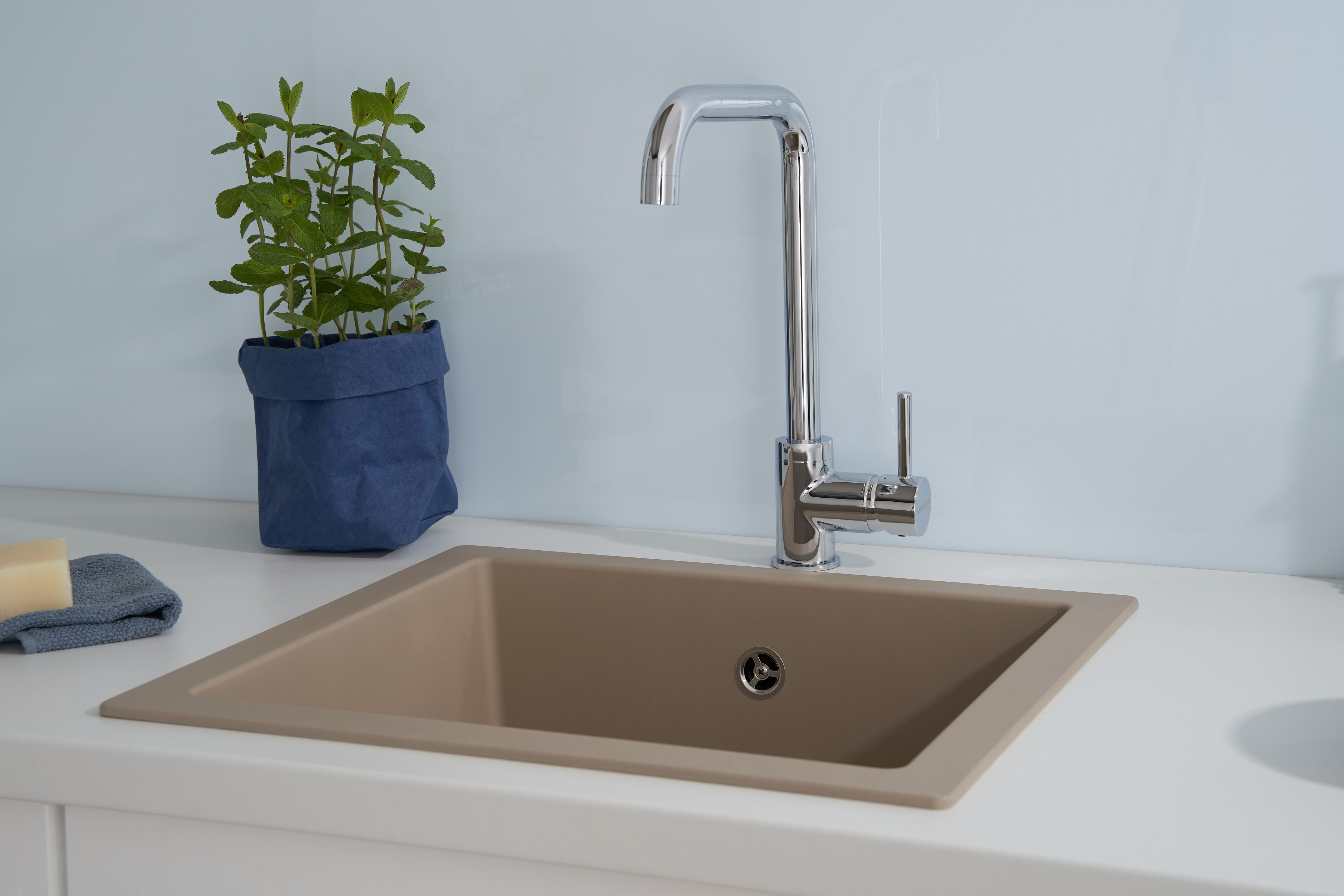 Küchenspüle mit Wasserhahn, Minzepflanze, Seife und blauem Handtuch.