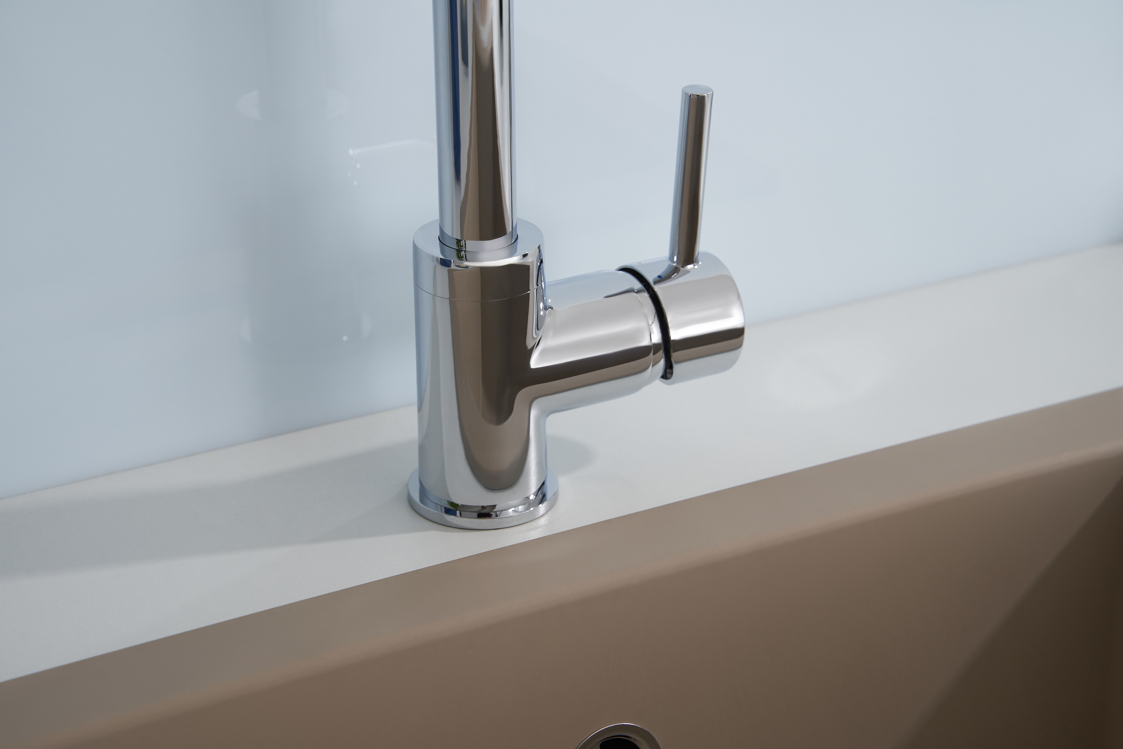 Chromarmatur über einer beigen Arbeitsplatte und Spüle, weißer Wandhintergrund. Sauberes, modernes Design.