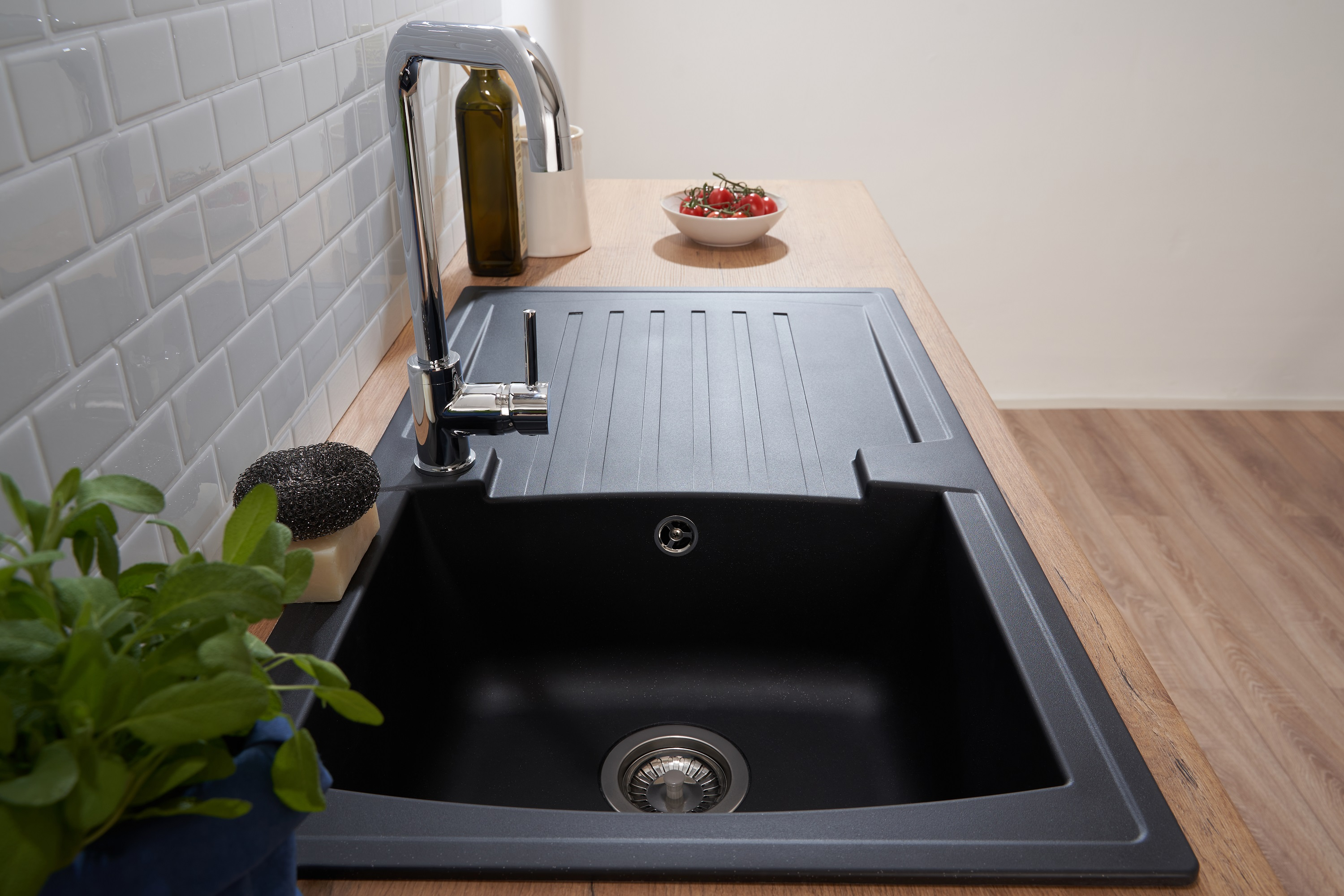 Schwarzes Küchenbecken mit Wasserhahn, Pflanze und Tomatenschale auf Holz-Arbeitsplatte.