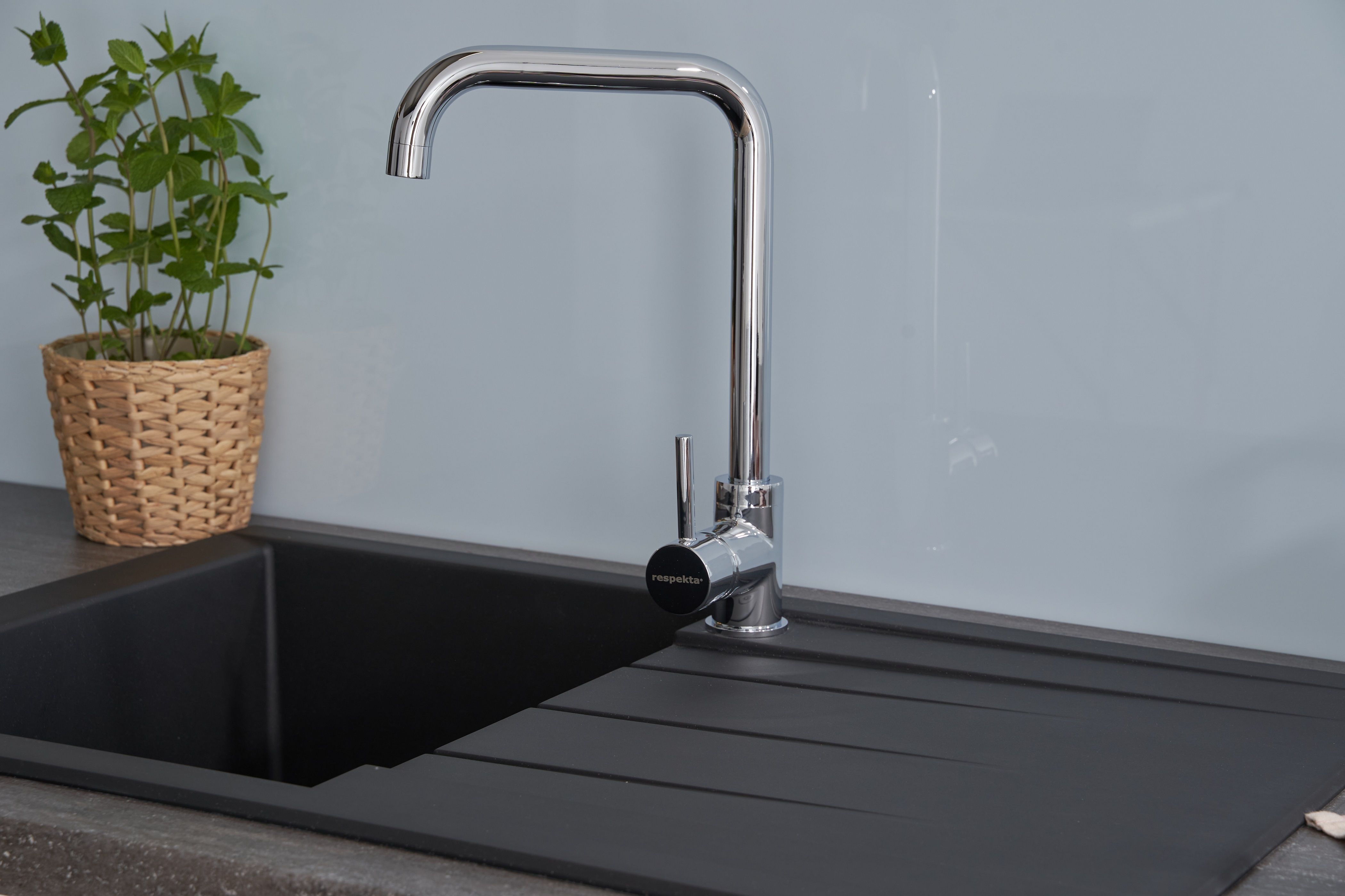 Moderner Küchenhahn mit schwarzem Waschbecken und kleiner Pflanze im Weidenkorb.