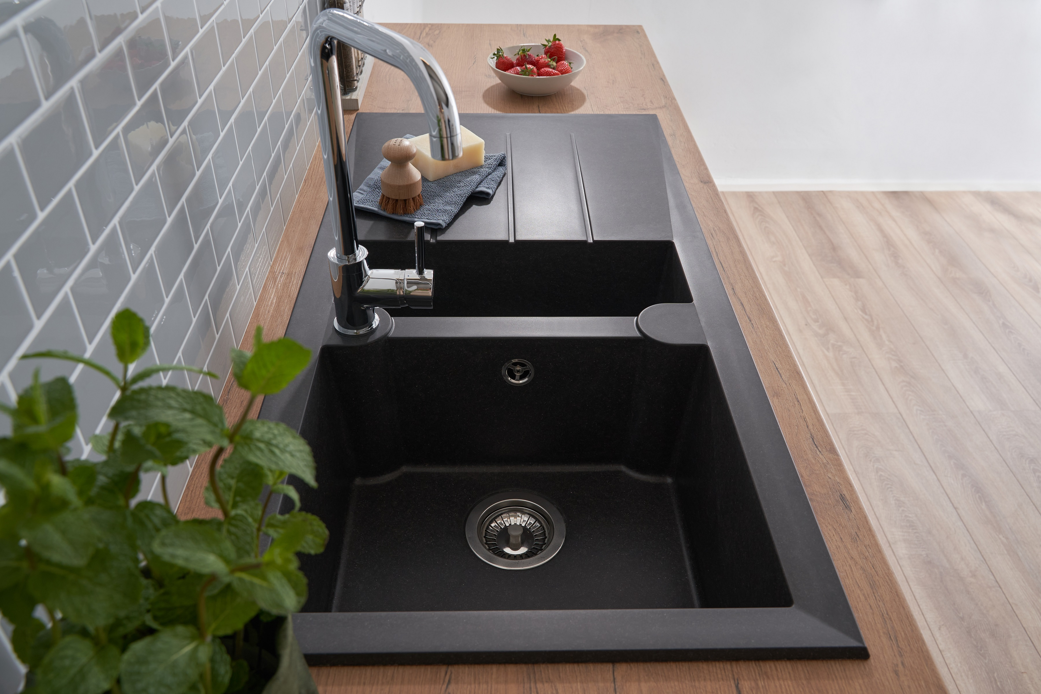 Schwarzes Küchenbecken mit Chromarmatur, Erdbeeren und Pflanze auf Holz-Arbeitsplatte.