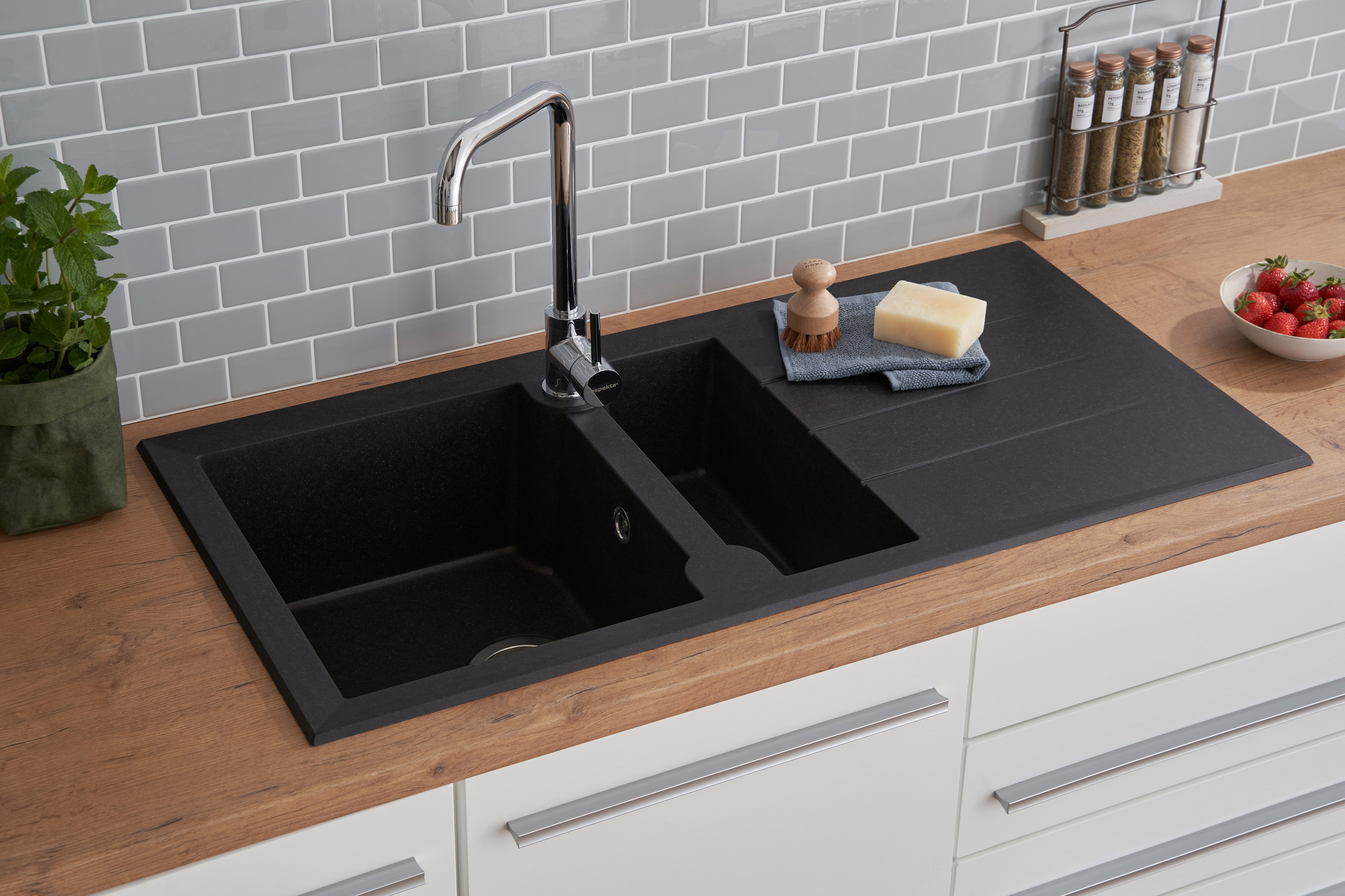 Schwarzes Küchenbecken mit Wasserhahn, Seife und Erdbeeren auf einer Holztheke.