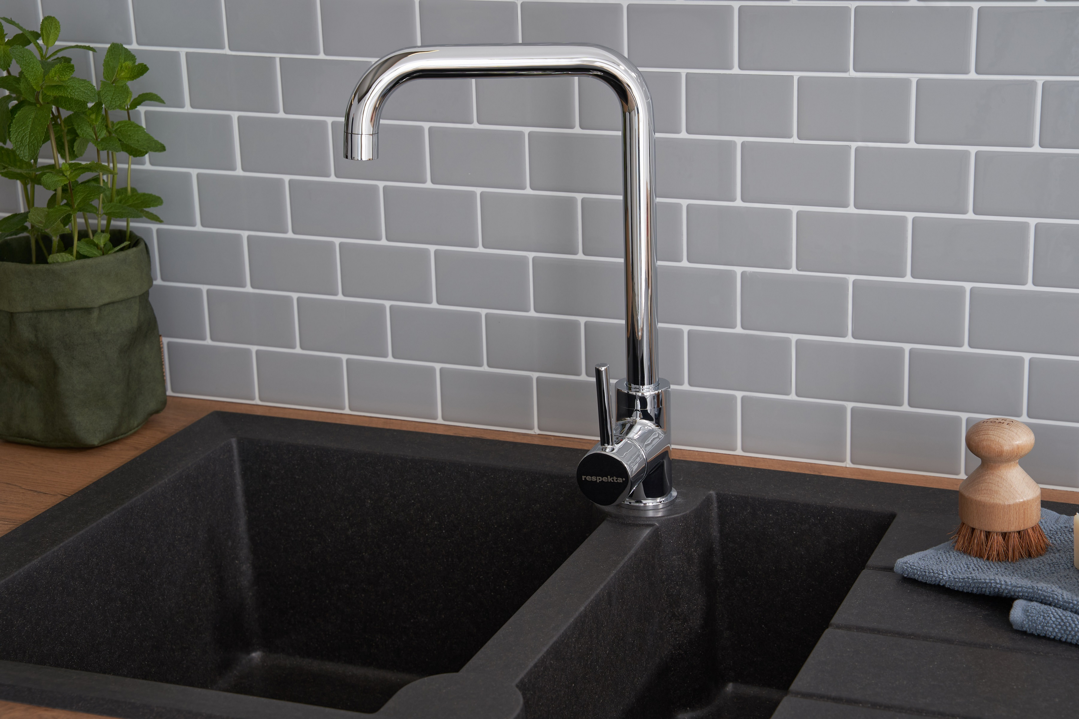 Küchenspüle mit Chromarmatur, schwarzem Waschbecken und einer grünen Pflanze im Topf.